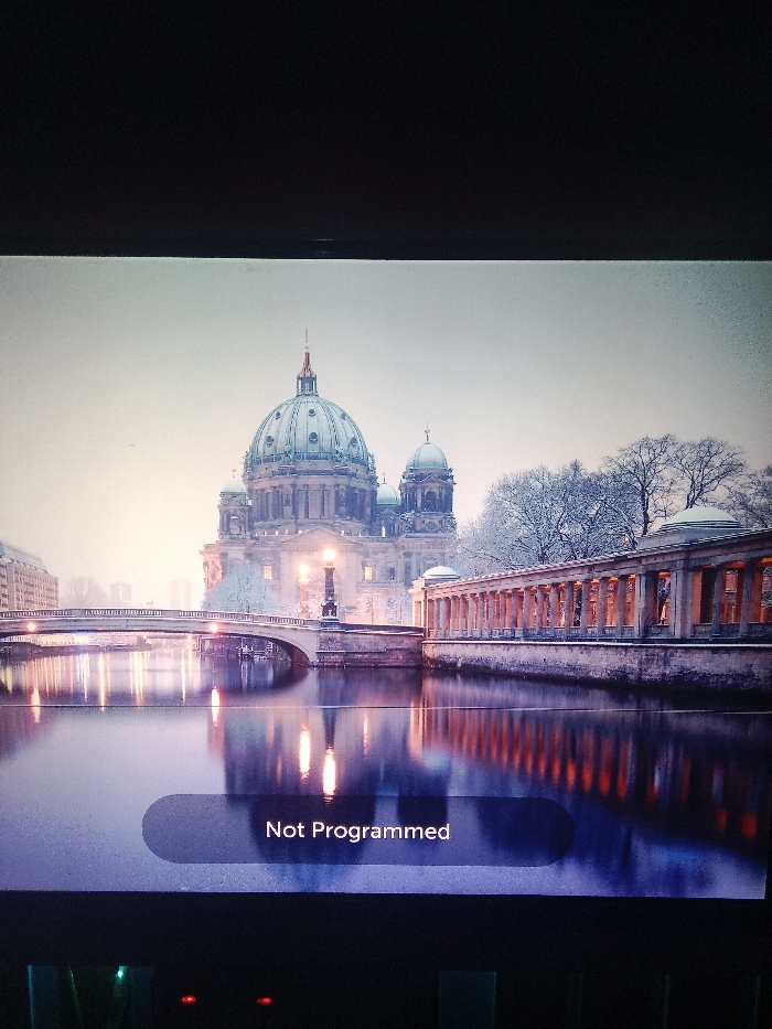 A serene winter scene depicts the Berlin Cathedral reflected in the Spree River. A bridge connects to the colonnaded Old National Gallery. Snow dusts the architecture and trees, adding to the tranquil atmosphere. An LG television displays the image with a "Not Programmed" message. The room is dark, with the TV screen providing the main light source.