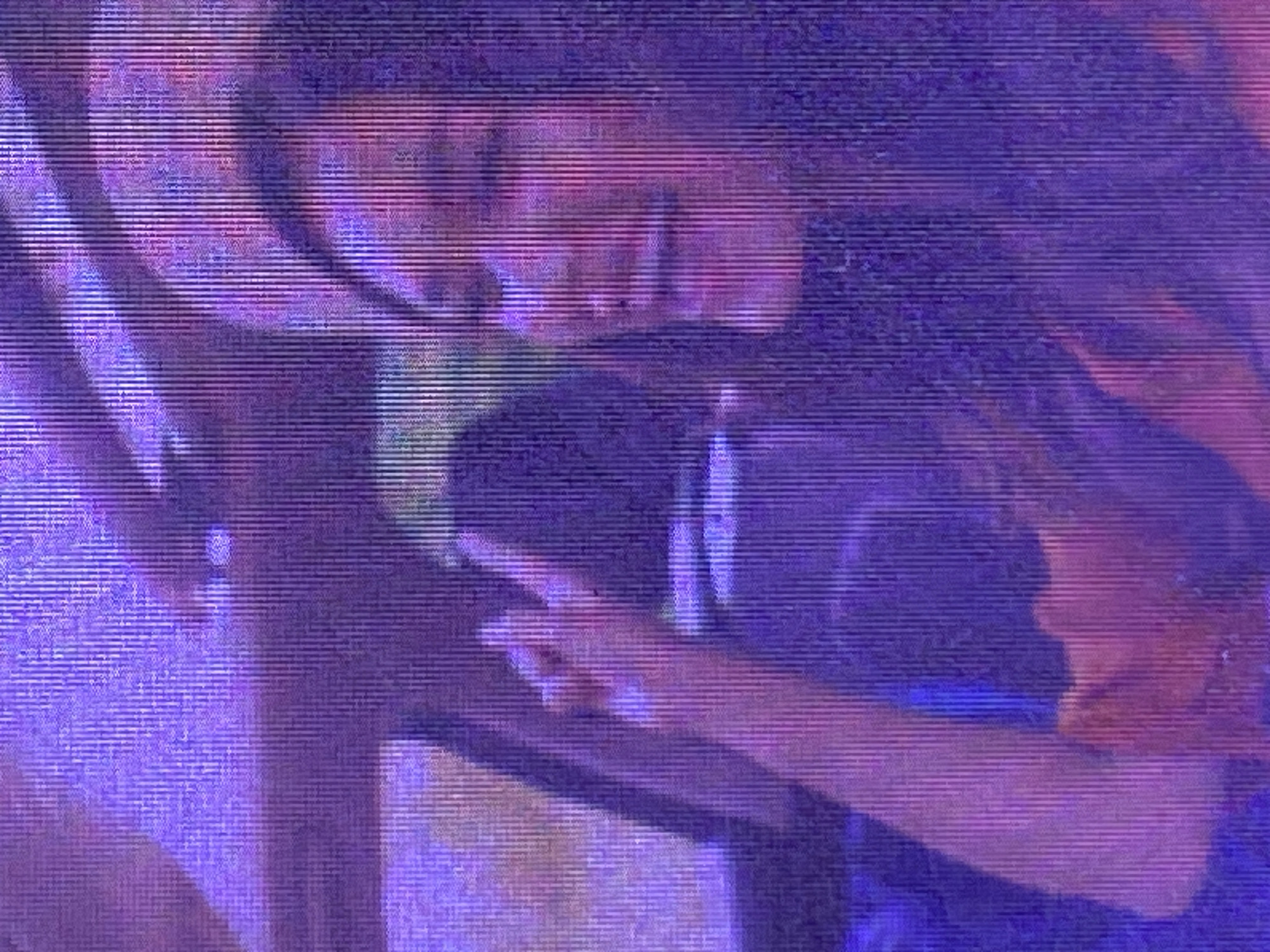 The image captures a close-up, low-resolution, and heavily distorted view of two individuals, likely embraced in an intimate moment. The subjects are bathed in purple and pink light, which, combined with the digital noise and horizontal lines across the frame, gives the scene a surreal, almost dreamlike quality.
One individual's face is partially visible, turned towards the other, with their lips slightly parted. Their hand is extended, possibly touching the other person's face or hair. The other individual's face is more obscured, but their head is tilted, suggesting closeness and comfort. They are both dressed in dark clothing.
The setting appears to be indoors, possibly at night, given the artificial lighting and the lack of any discernible natural elements. The overall mood is intimate and sensual. The low quality of the image makes it difficult to identify specific objects or details about the location beyond the presence of the two people and the lighting. There is no visible text in the image. The context of Ikorodu, Nigeria, is not directly evident from the visual information presented.