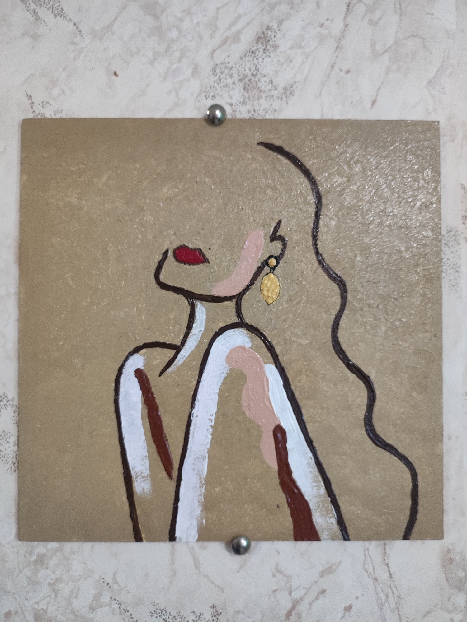 The image shows a framed painting of a woman's profile against a textured, tan background. The woman is depicted with a simple, dark outline. Her lips are painted red, and she wears a gold earring. Her body is rendered with strokes of white and light pink paint, suggesting clothing or skin. The painting is affixed to a wall with two silver tacks, one at the top and one at the bottom, slightly off-center. The wall has a light-colored, patterned wallpaper. The painting is approximately square in shape and appears to be made of acrylic or oil paint on a solid surface. The image provides no information about the location in Cherkasy, Ukraine.