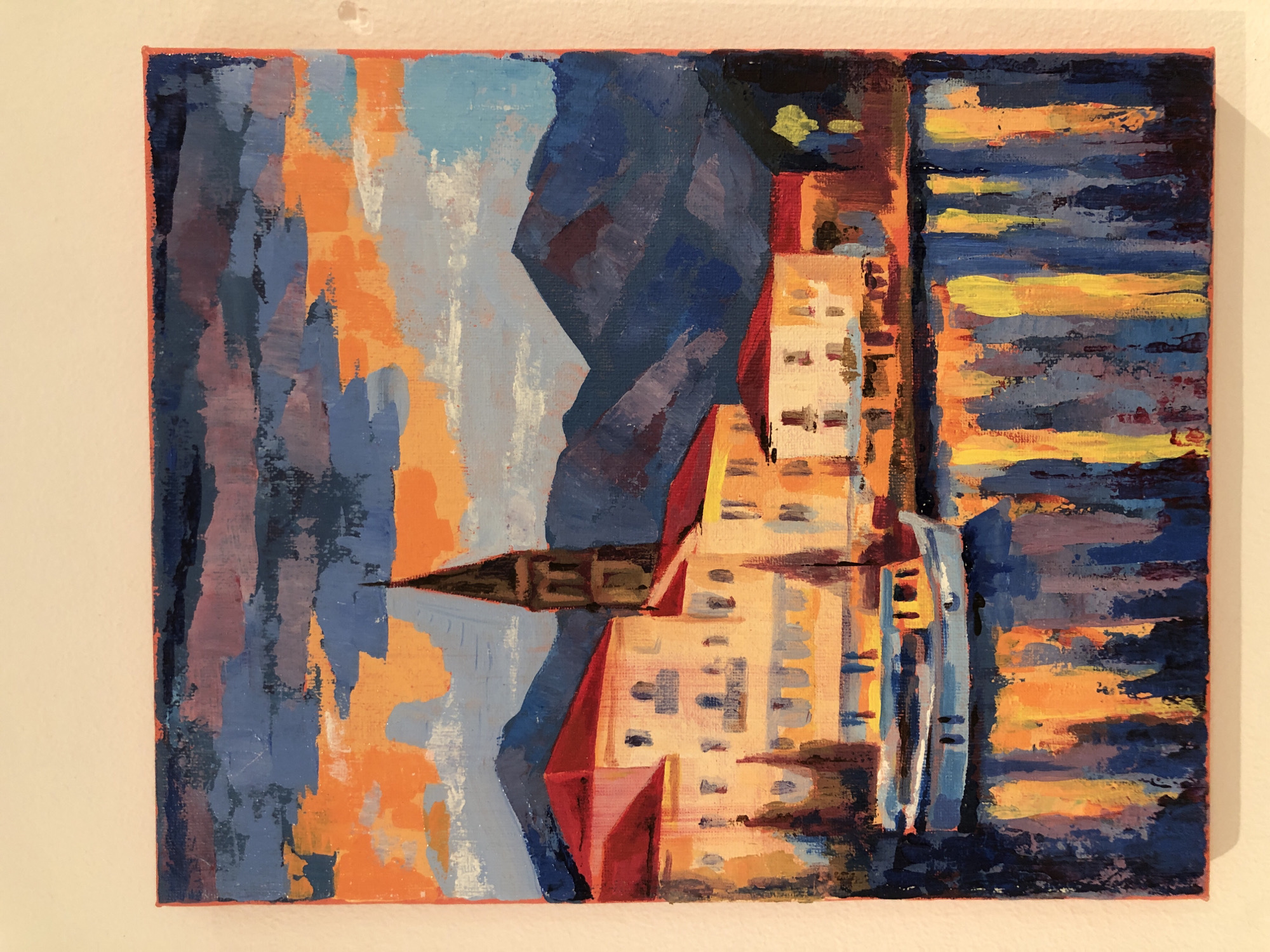 This is a vertical acrylic painting on canvas depicting a city scene in València, Spain. The style is impressionistic, with thick brushstrokes and a vibrant color palette dominated by blues, oranges, yellows, and reds. The painting appears to represent buildings, possibly apartments or hotels, rendered in abstract shapes and colors. The left side of the painting features large blocks of blue and orange, with lighter blue and white strokes suggesting sky or perhaps water. A dark, pointed shape, possibly a steeple or a stylized building, juts out from the center left. To the right, a cluster of buildings with illuminated windows is depicted in shades of yellow, orange, and white. The rightmost portion of the painting is a stylized representation of a body of water, likely the Mediterranean Sea, with horizontal bands of dark blue, yellow, and orange, evoking the reflection of lights or the sunset. The overall impression is that of a lively urban environment, possibly at dusk or dawn given the warm and cool color contrasts. No text is visible in the image.