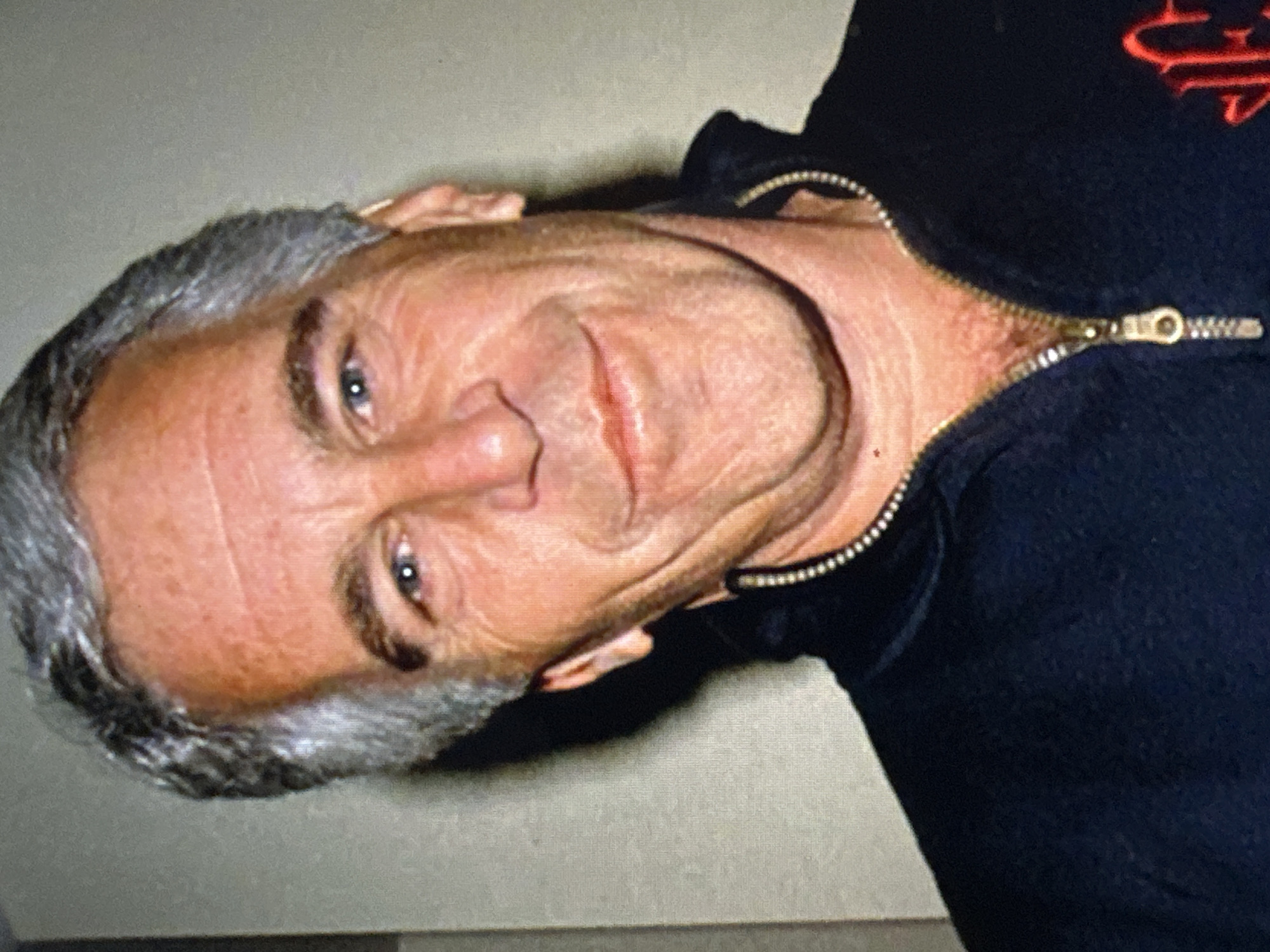An image depicts a close-up of an older man with grey hair, wearing a dark zip-up jacket with a visible zipper. The location, Donji Pobori, Montenegro, is not discernible from the image itself.