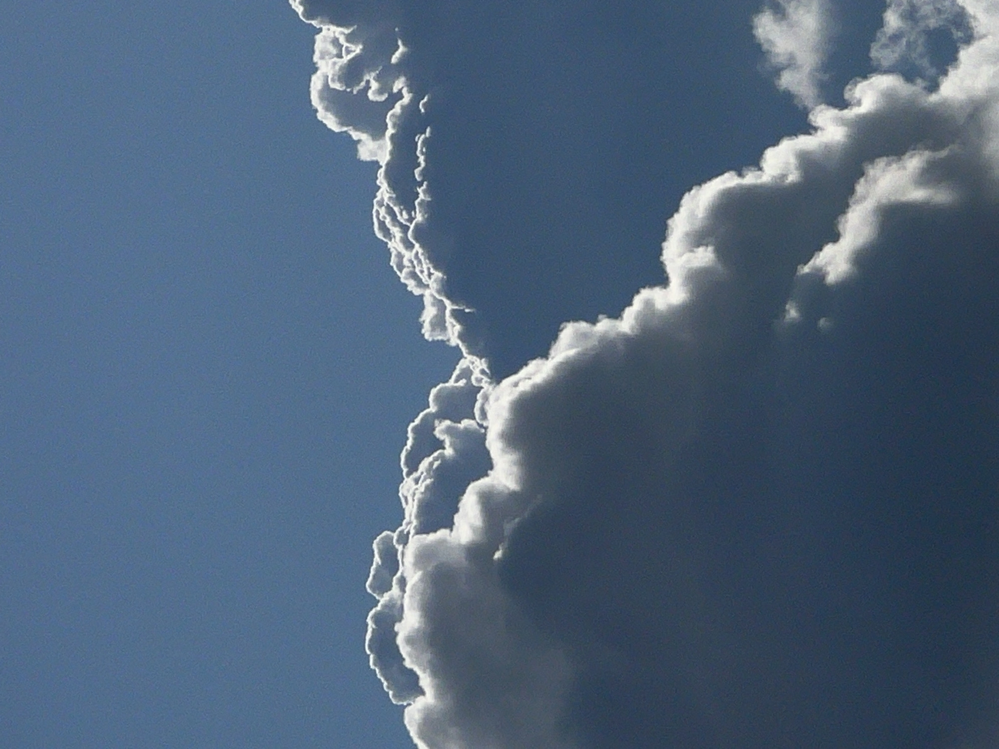 The image shows a close-up view of cumulus clouds against a clear blue sky. The clouds are white and puffy with shadowed undersides, indicating sunlight illuminating them from above and to the side. The scene appears to be an outdoor environment, likely taken during daylight hours, depicting a section of the sky with prominent cloud formations. There are no people, animals, or man-made structures visible in the frame. The setting could be anywhere with clear weather and cloud cover, and the specific location in Большой Букор, Russia, cannot be determined from the visual information alone.
