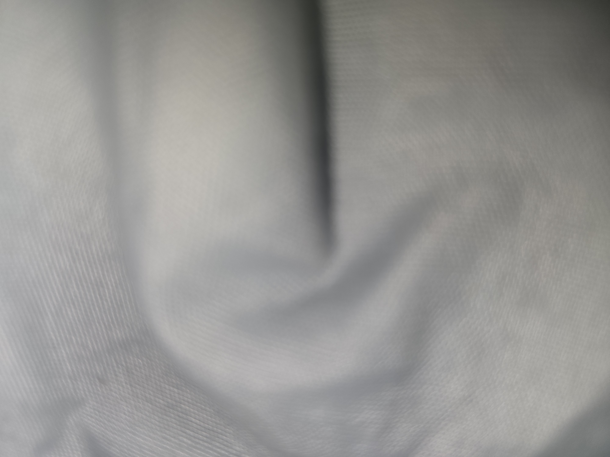 The image is a close-up, abstract view of a light-colored, textured fabric. The fabric appears to be folded or draped, creating soft shadows and highlights that give it a sense of depth. The texture of the fabric is visible as a fine, repeating pattern, possibly a weave. The lighting is diffuse, contributing to the soft, muted tones of the image. There are no discernible objects, people, or environmental details that would suggest a specific location, including Ulan-Ude, Russia. The image is purely focused on the visual characteristics of the fabric itself.