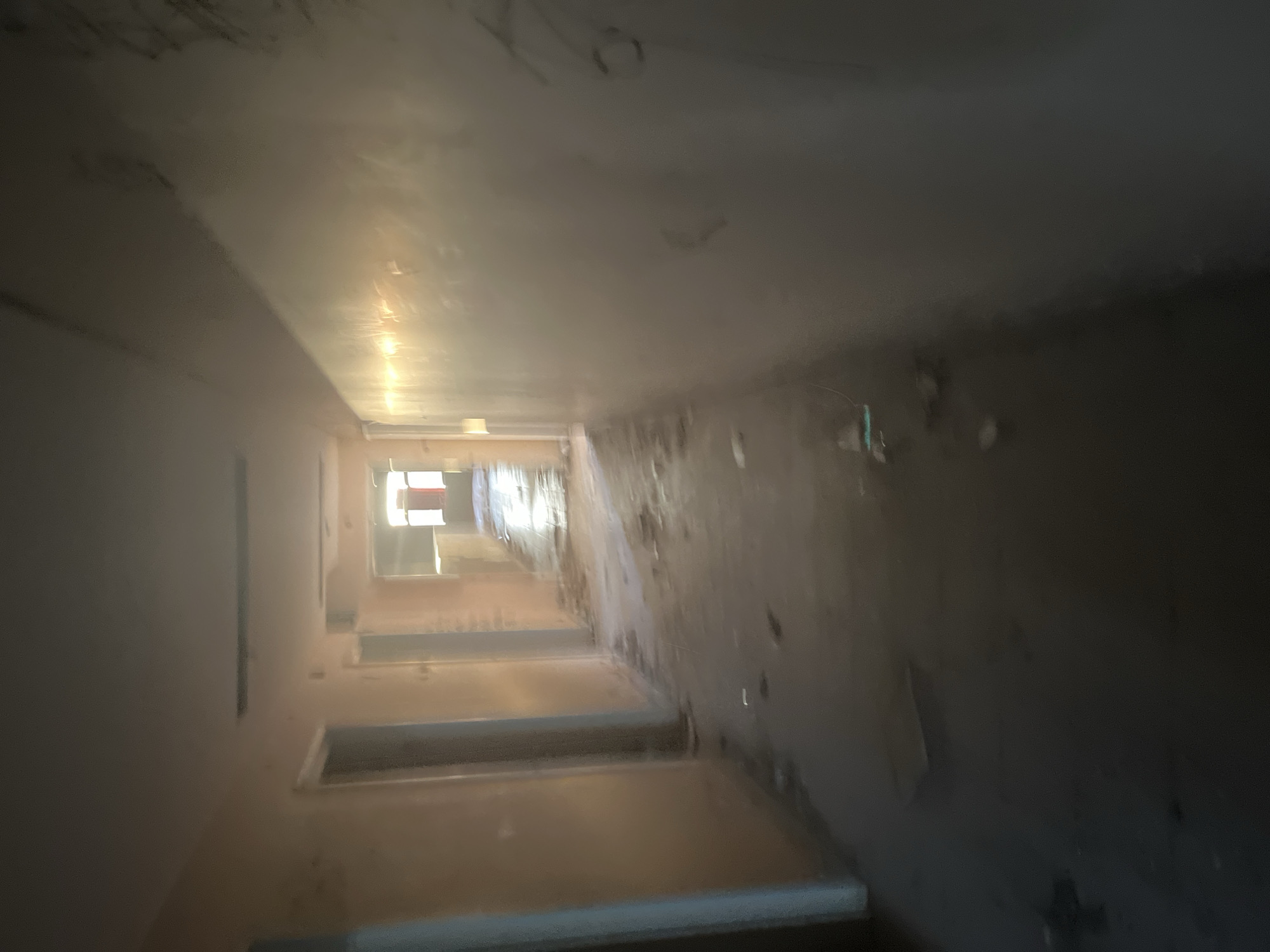 The image shows a dilapidated hallway in a building in the city of Марковский, Russia. The hallway appears long and narrow, with walls showing signs of decay, including peeling paint and dirt. There are doorways visible along the hallway, suggesting possible rooms or offices. The lighting is dim, with sunlight coming from a window at the end of the hallway. The overall impression is that the building is abandoned or neglected. There are no people visible in the scene.