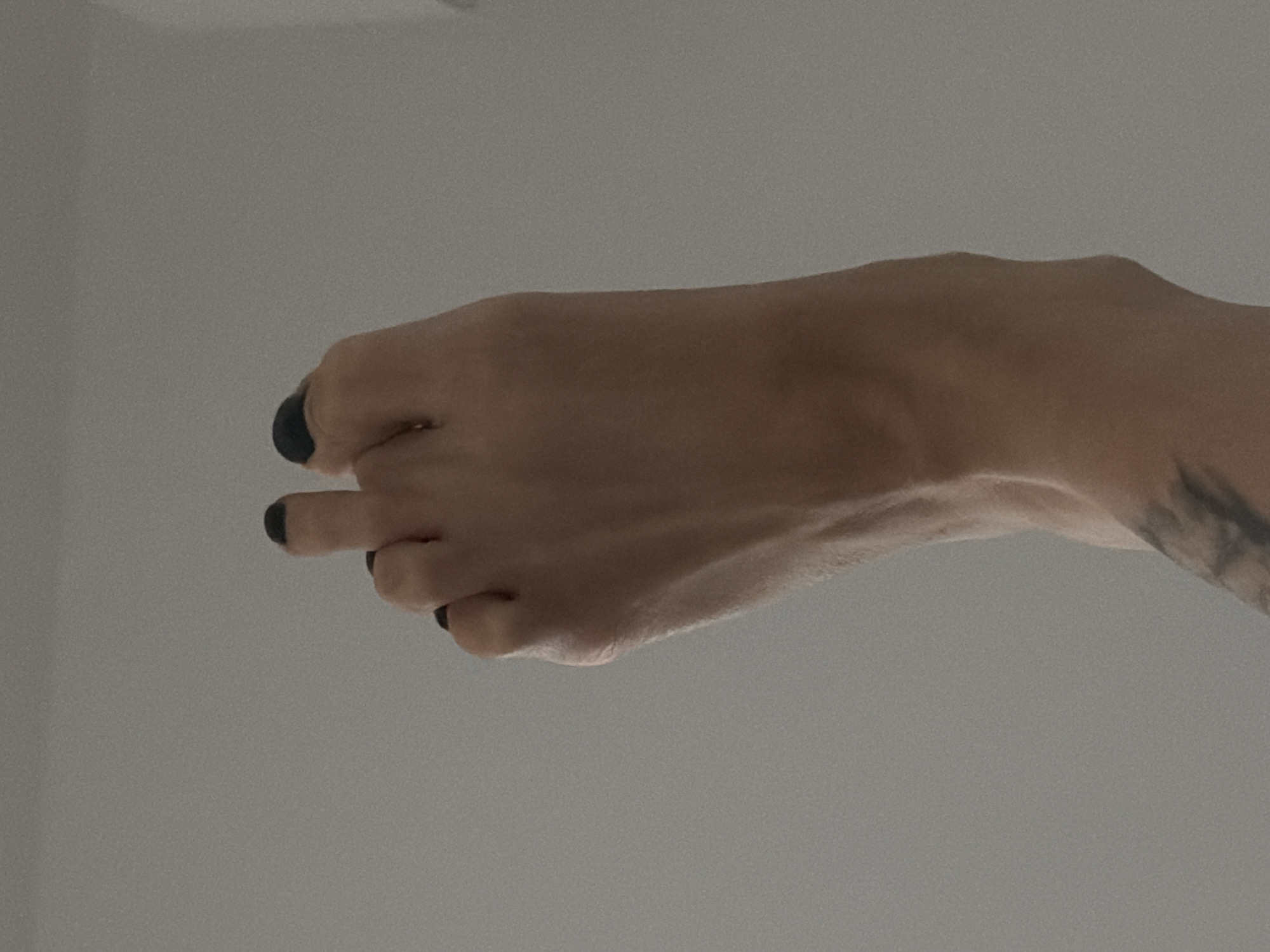 A close-up shot shows a light-skinned human hand with painted black nails, oriented horizontally against a neutral gray background. The wrist displays a portion of a tattoo. No specific location or context relates the image to Đà Nẵng, Vietnam.