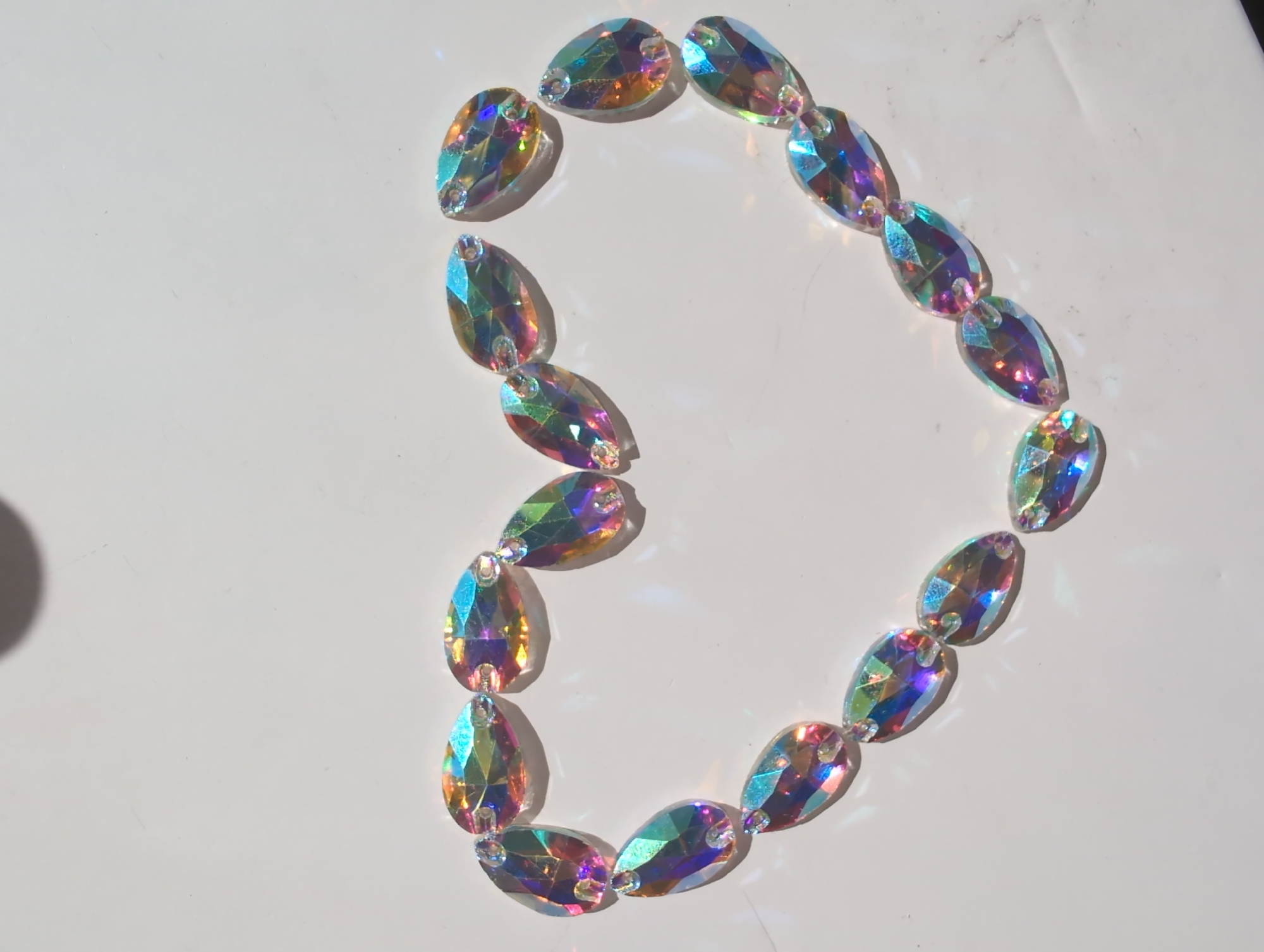 The image shows a collection of iridescent teardrop-shaped beads arranged in a roughly circular shape resembling the letter "D" or the number "3" on a white surface. The beads are facing different directions. There are no indications of a specific location such as Izhevsk, Russia, or people, actions, or interactions in the image. The environment is a plain white surface.