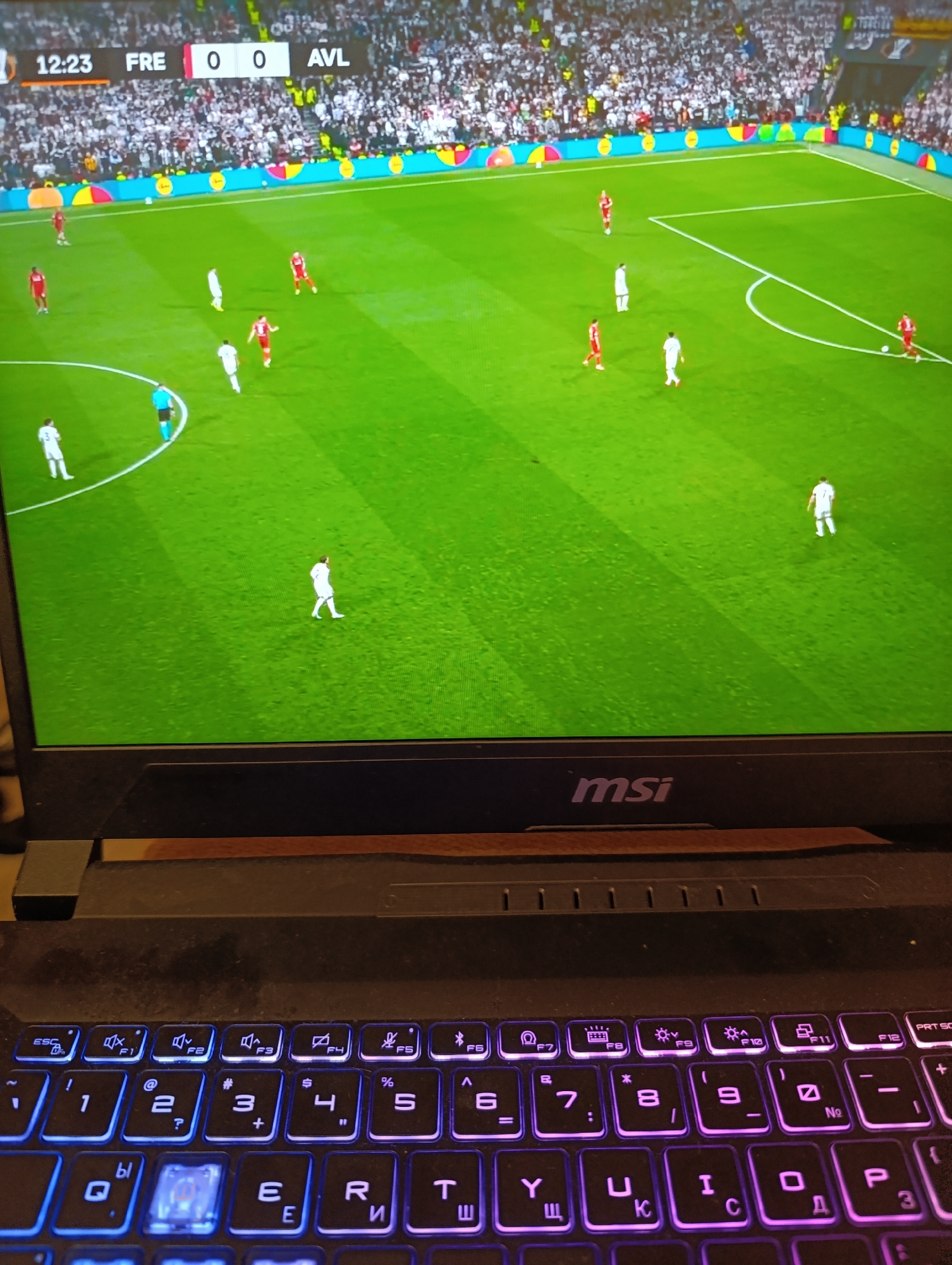 A close-up image shows a laptop with a soccer video game displayed on its screen. The laptop is an MSI brand. The game's score is FRE 0, AVL 0, and the game clock shows 12:23. The laptop keyboard is visible, with keys illuminated in blue and purple. The layout appears to be a QWERTY keyboard. The image provides no information related to the city of Plovdiv, Bulgaria.