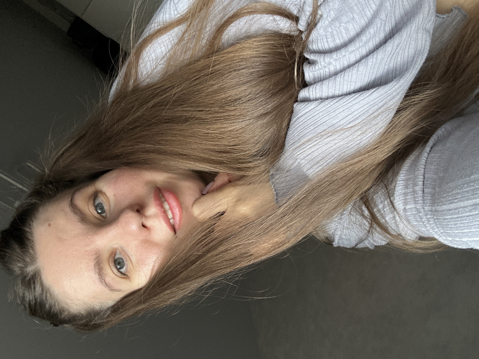 A woman with light brown hair and light eyes is shown in a close-up shot. She is wearing a light blue ribbed top. Her hand is near her face. The background appears to be a dark, neutral color. The location, Klin, Russia, is not evident from the image.