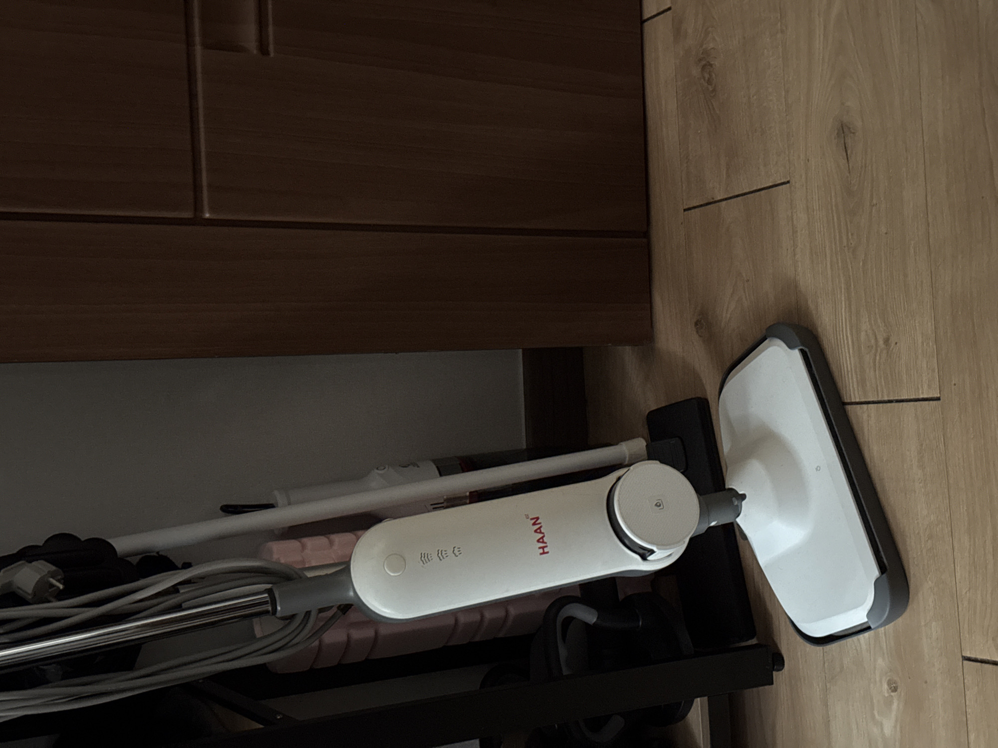 The image shows a white HAAN steam mop leaning against a wooden floor and a cabinet. The mop is partially obscured by a black rack. The scene appears to be indoors. The location in Hwaseong-si, South Korea, cannot be determined from the image.