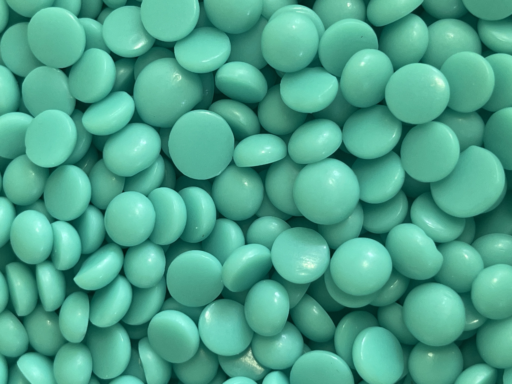 The image is a close-up, overhead shot of a pile of small, round, teal-colored objects. The objects are smooth and appear to be made of a solid material, possibly candy or small wax beads. They are densely packed together, creating a textured surface. The lighting is even, and there are no shadows. The background is entirely filled with these objects. There is no discernible city or specific location information, including Kyiv, Ukraine, visible in the image.