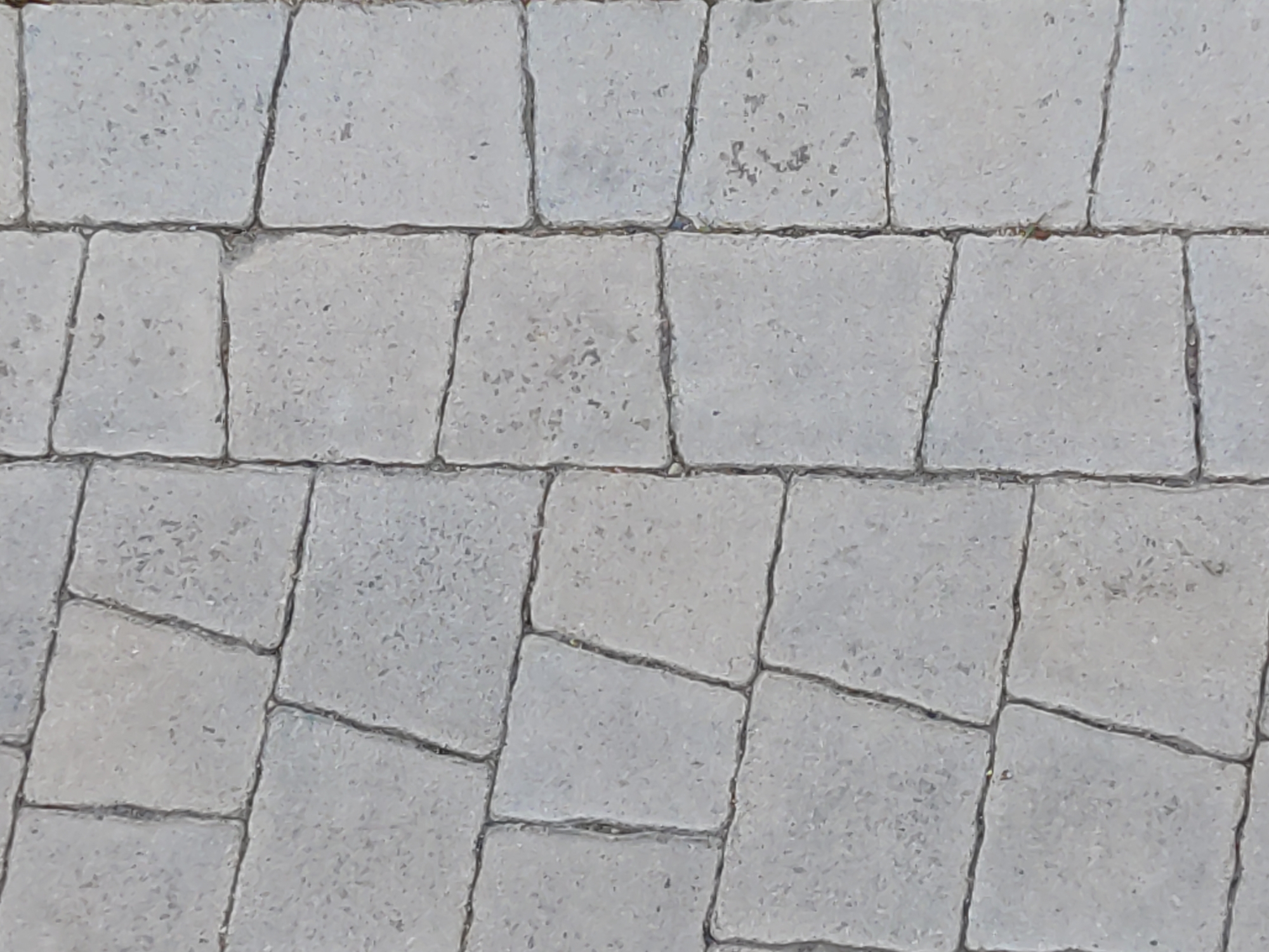 The image shows a close-up, overhead view of a paved surface composed of light gray, rectangular stone pavers. The pavers are arranged in an irregular pattern, with varying widths and lengths, and are separated by dark, thin grout lines. The surface appears to be outdoors, possibly a pathway or patio. There are no people or animals visible in the image, and no specific landmarks or structures are identifiable to pinpoint a location within Бараўлянскі сельскі Савет, Belarus. The lighting suggests it is daytime.