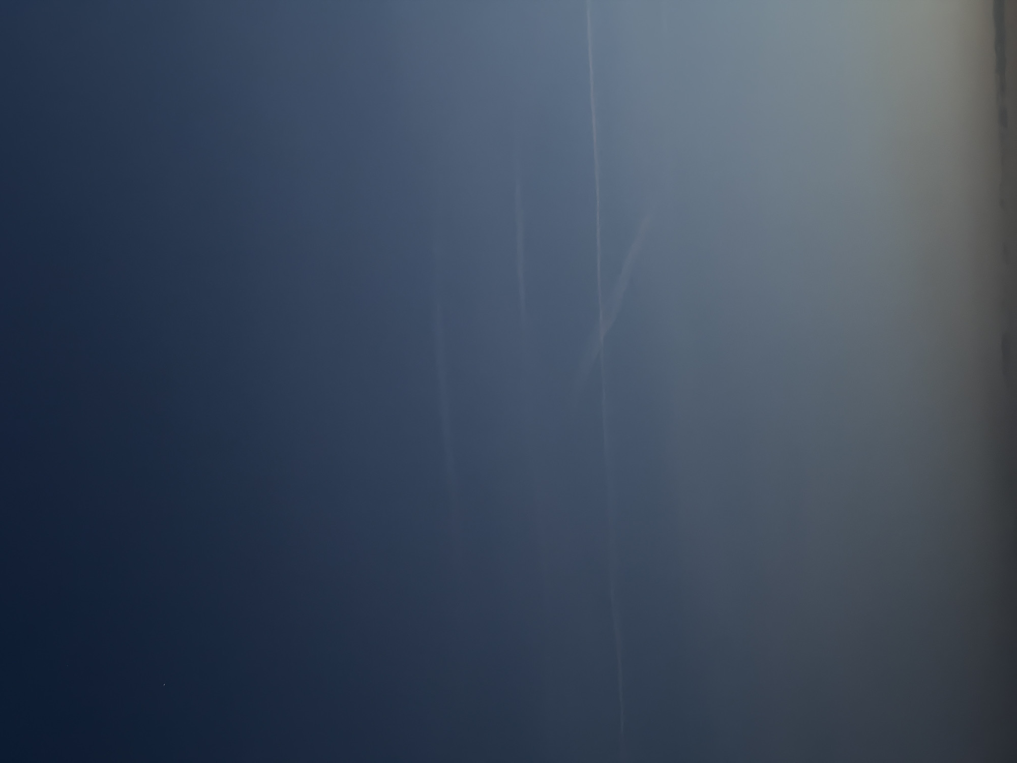 The image shows a predominantly blue sky with faint contrails of airplanes crisscrossing each other. The right side of the image transitions into a lighter, almost white, cloudy area. The overall scene is hazy. The location is most likely Nizhny Novgorod, Russia based on the instructions.