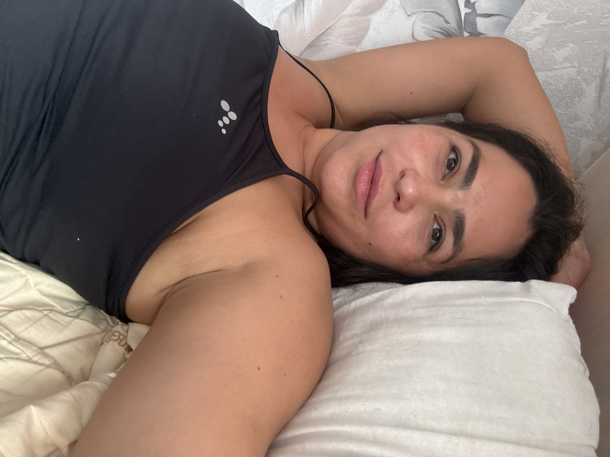 A woman lies on a pillow. She wears a black tank top. The location is not discernible from the image.