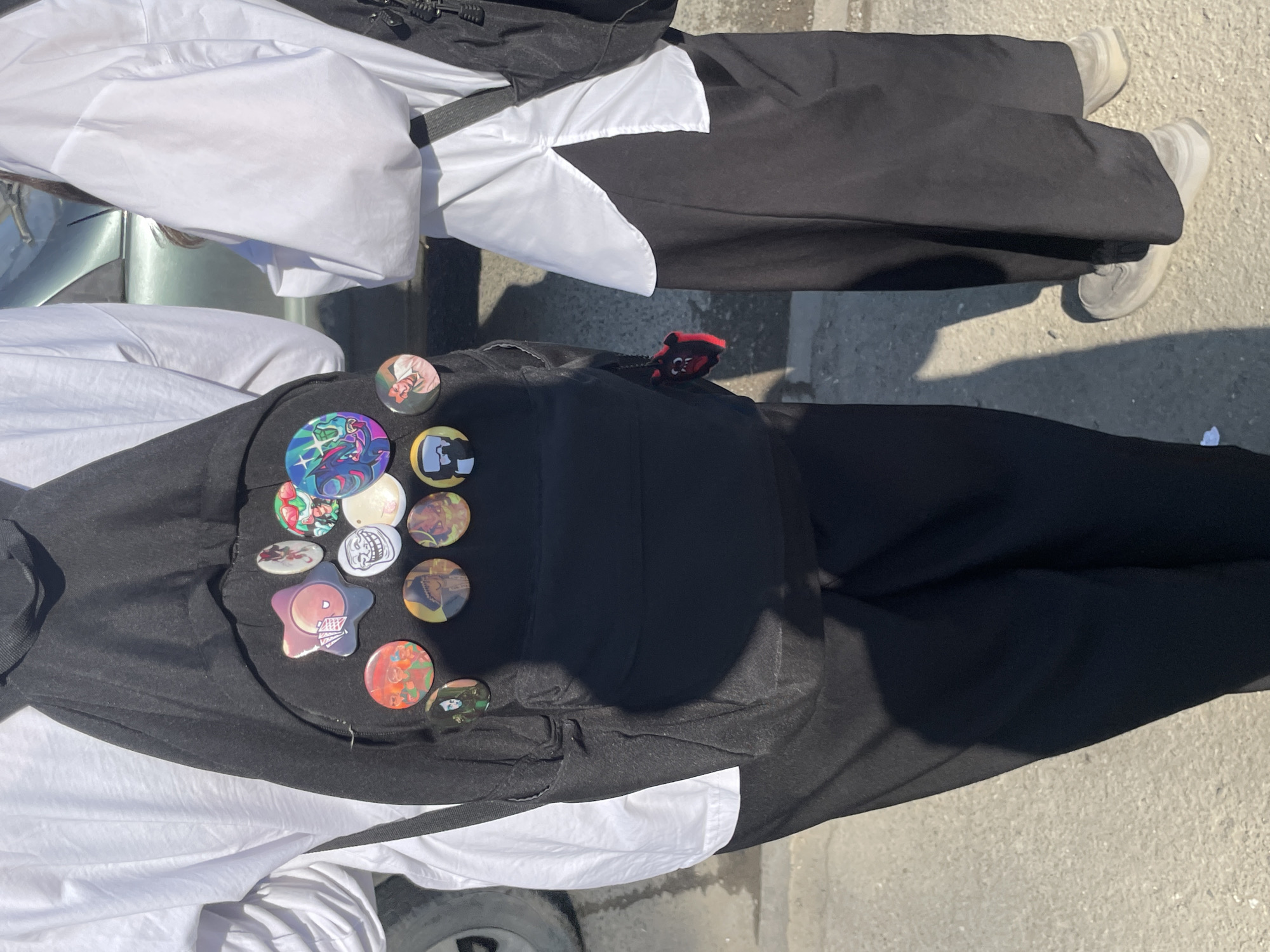 A view from above shows two individuals standing on a concrete surface. The person on the right wears black pants, a white shirt and light-colored shoes. The person on the left is dressed similarly, with black pants and a white shirt. The person on the left has a collection of pins on the front of their garment.
The image does not contain enough information to determine the location in the city of Izhevsk, Russia.