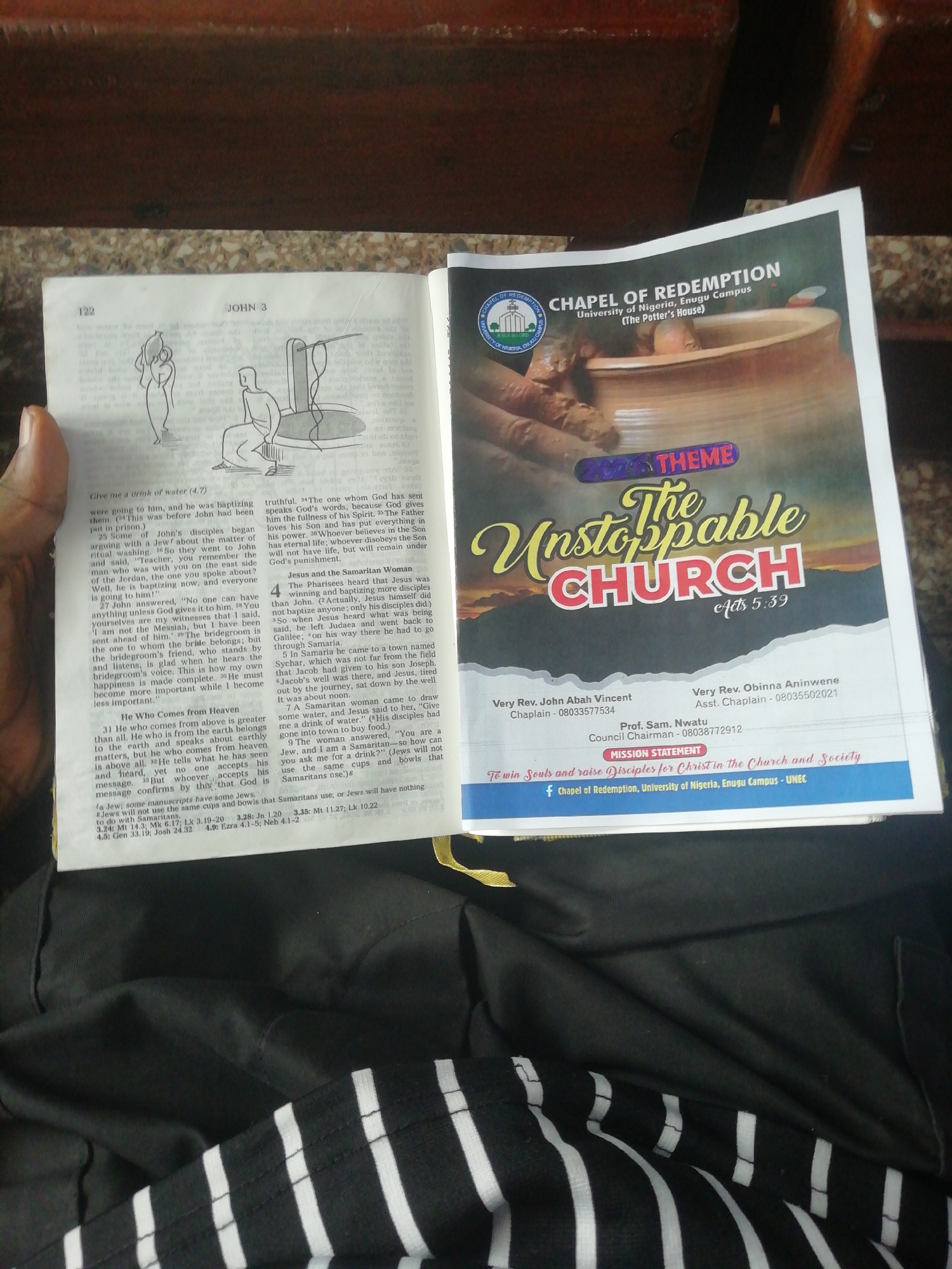 The scene shows an open Bible on the left page, and a church program on the right page. The Bible is opened to John 3, with a drawing of Jesus and the Samaritan woman at the well. The church program is for the Chapel of Redemption, University of Nigeria, Enugu Campus, and advertises the theme "The Unstoppable Church". The Bible and program are resting on a person's lap wearing clothing with black and white stripes.