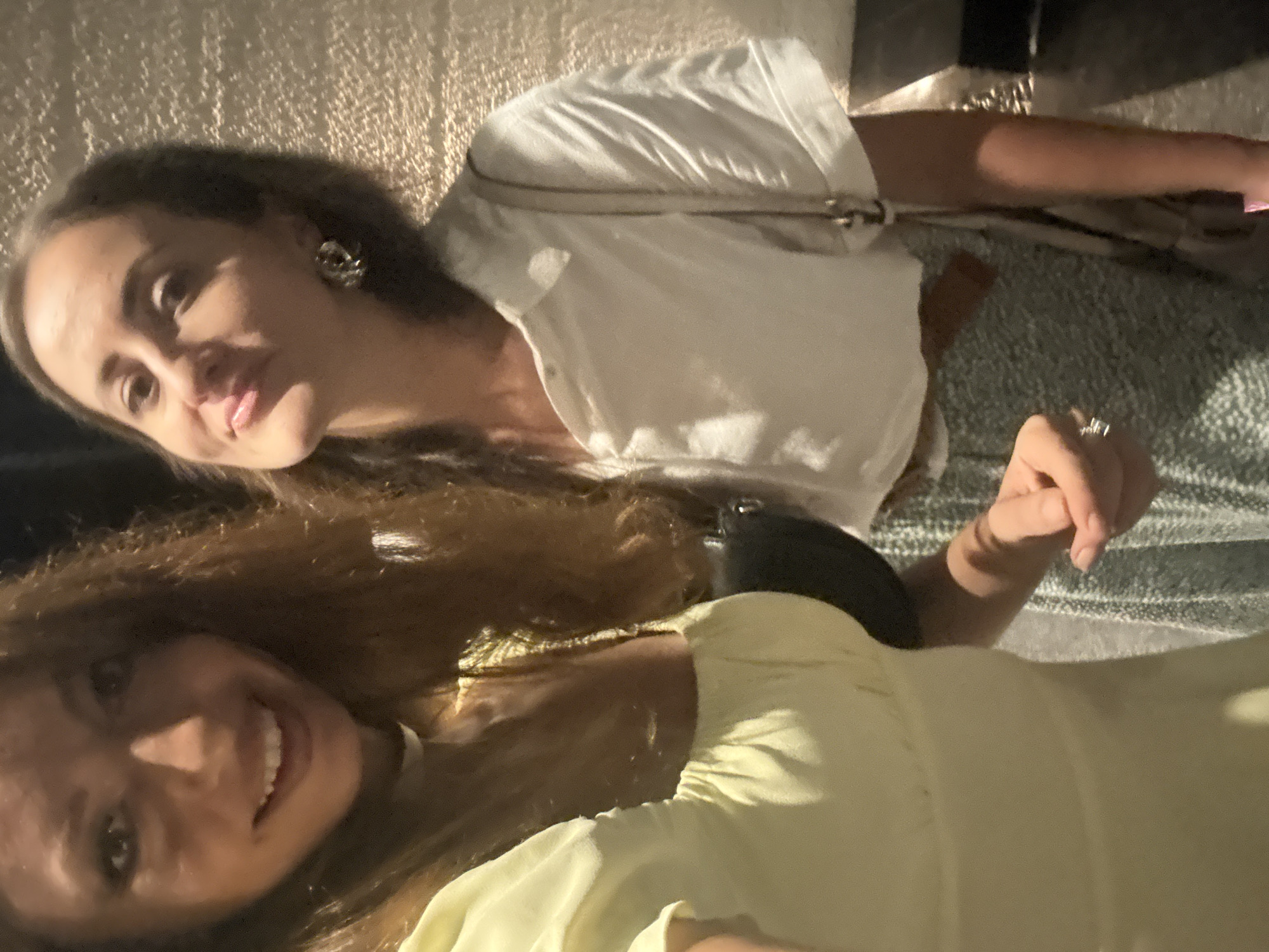 Two women are posing for a selfie indoors. One woman has light brown hair and is wearing a white shirt. The other woman has dark brown hair and is wearing a yellow shirt. It is unclear if this photo was taken in Baan Bo Phut, Thailand.