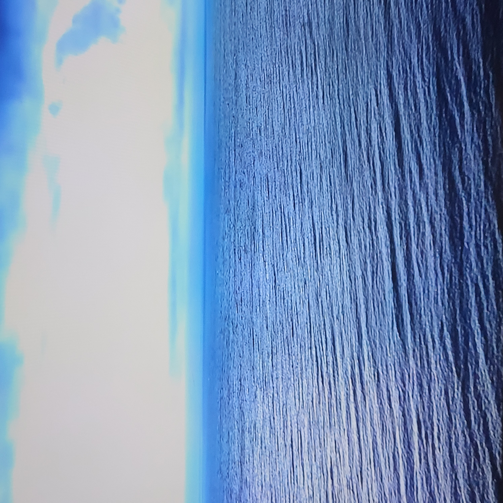 The image appears to depict a view of the sky and ocean or a large body of water, perhaps from an elevated vantage point. The left side of the frame shows bright light with blue and white clouds, while the right side features a textured blue surface that could be the ocean. The perspective is slightly tilted. There are no discernible people, subjects, objects, actions, or interactions in the image. There's no evidence this image is from or related to Yerevan, Armenia.