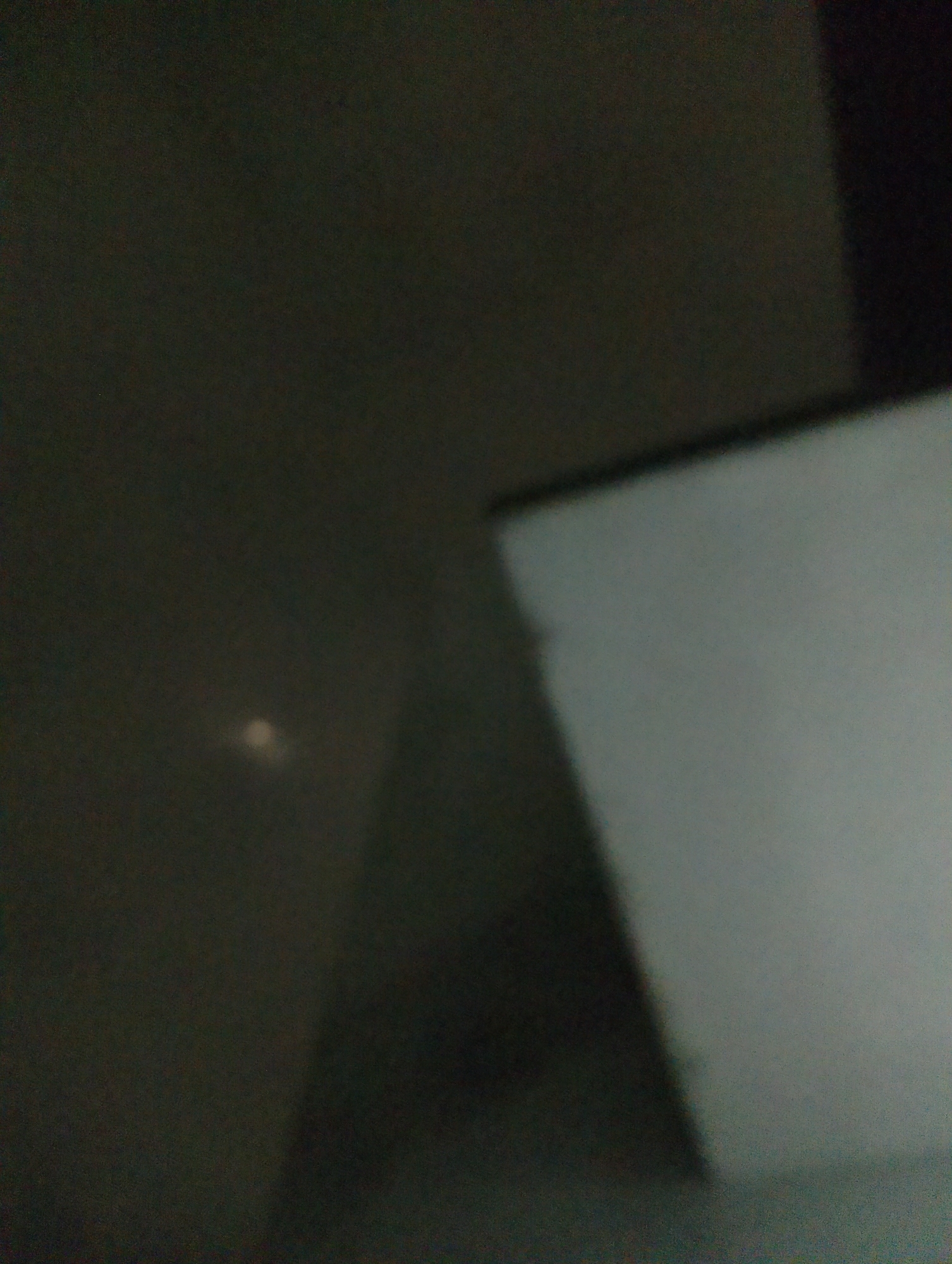 The image shows a dimly lit interior space. In the foreground, a large, light-colored surface, possibly a wall or a screen, occupies the right side of the frame. The left side of the image is darker and appears to be a wall. There is a small, blurry, luminous spot in the darker area, the nature of which is unclear. The overall scene is out of focus, making it difficult to discern specific details. Without additional context or clearer imagery, it is not possible to determine the location within Magelang, Indonesia.