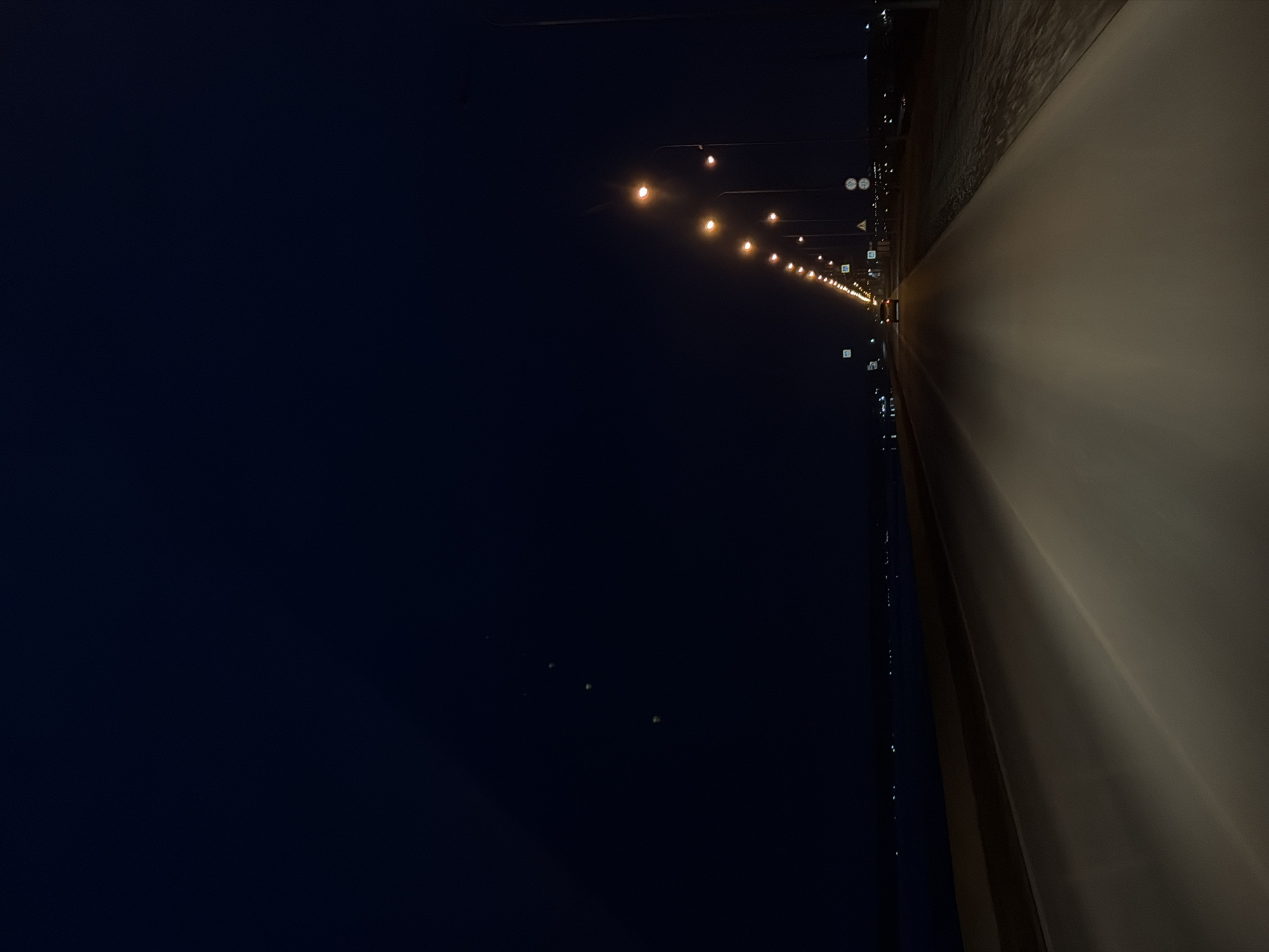 The image depicts an artificially illuminated bridge at night. Streetlights line the edge of the bridge. To the left of the bridge is the night sky. Noviy, Russia is implied by the prompt.