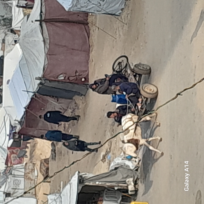 A displaced community is represented with makeshift tents in a dirt area. People are lying around the tents, and a small horse is pulling a cart loaded with items. A person is on the cart wearing a face mask. The scene depicts poverty and struggle.