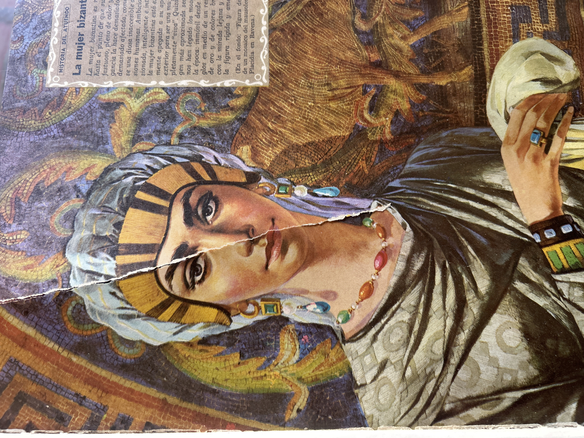 The image shows a ripped page from a magazine, likely an art history publication, featuring a mosaic-style illustration of a Byzantine woman. The woman is depicted from the chest up, wearing a golden headdress with a blue and white striped veil. She has dark eyes, full lips, and is adorned with large, dangling earrings and a beaded necklace. Her clothing appears to be a draped, olive-green tunic with a subtle circular pattern.
To the right of the illustration, a section of text is visible, titled "HISTORIA DEL ATUENDO" and "La mujer bizantina". The text discusses Byzantine fashion and mentions a mosaic of the Mausoleum of Galla Placidia in Ravenna.
The background of the illustration depicts a vibrant mosaic pattern with shades of blue, purple, gold, and green, featuring stylized animal or mythical creature motifs. A large, golden, furry animal-like figure is partially visible behind the woman.
The image's condition indicates it is torn down the middle, with the left side slightly overlapping the right. The edges are rough and show signs of wear. The image does not depict any elements that can be used to identify its location in Santa Ana, Venezuela.