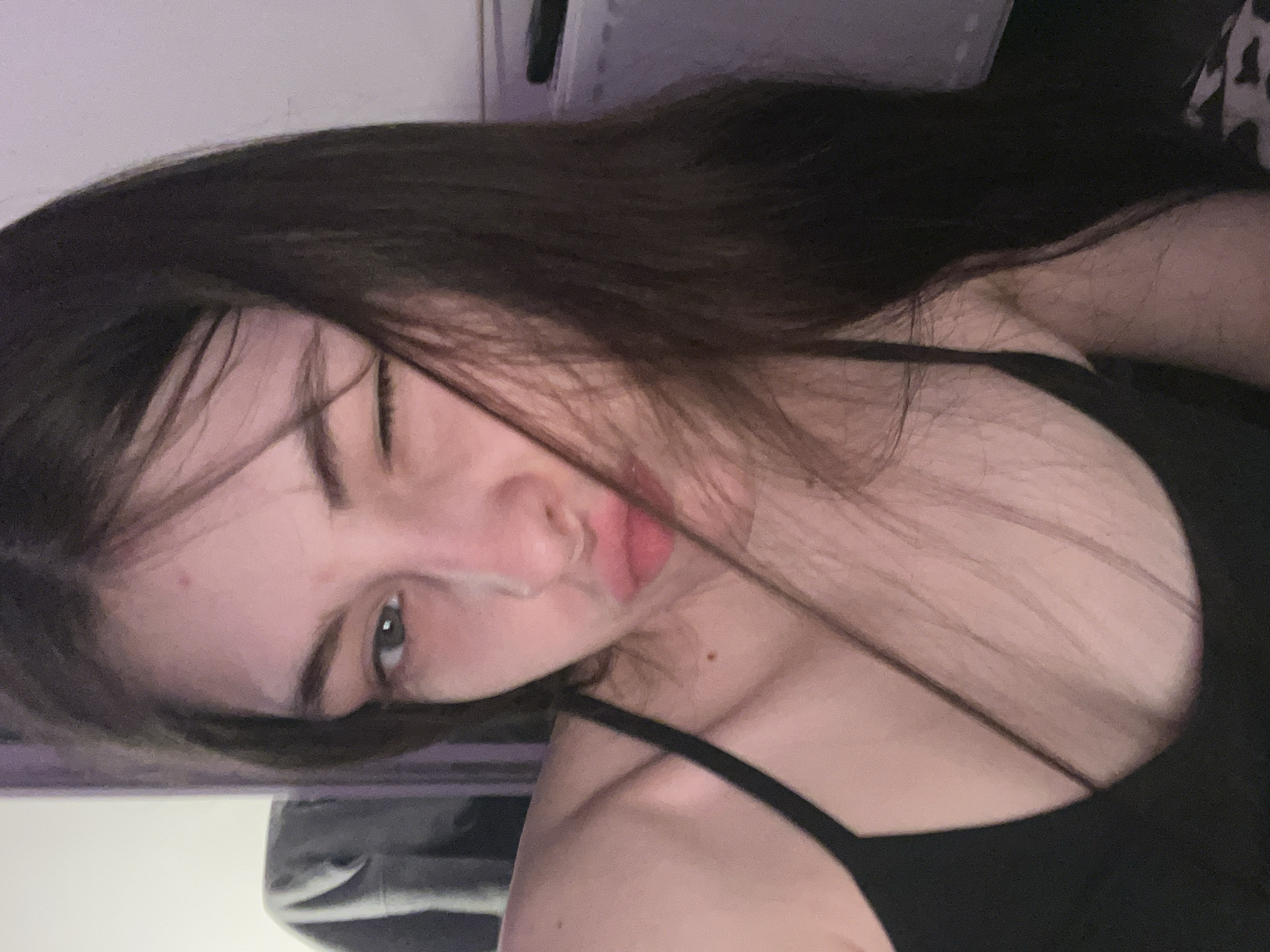A young woman with long dark hair and light skin is captured in a selfie. She is wearing a black tank top. She is squinting one eye and making a kissing face. The background is blurry and indistinct, making it impossible to determine a specific location in Saint Petersburg or anywhere else.