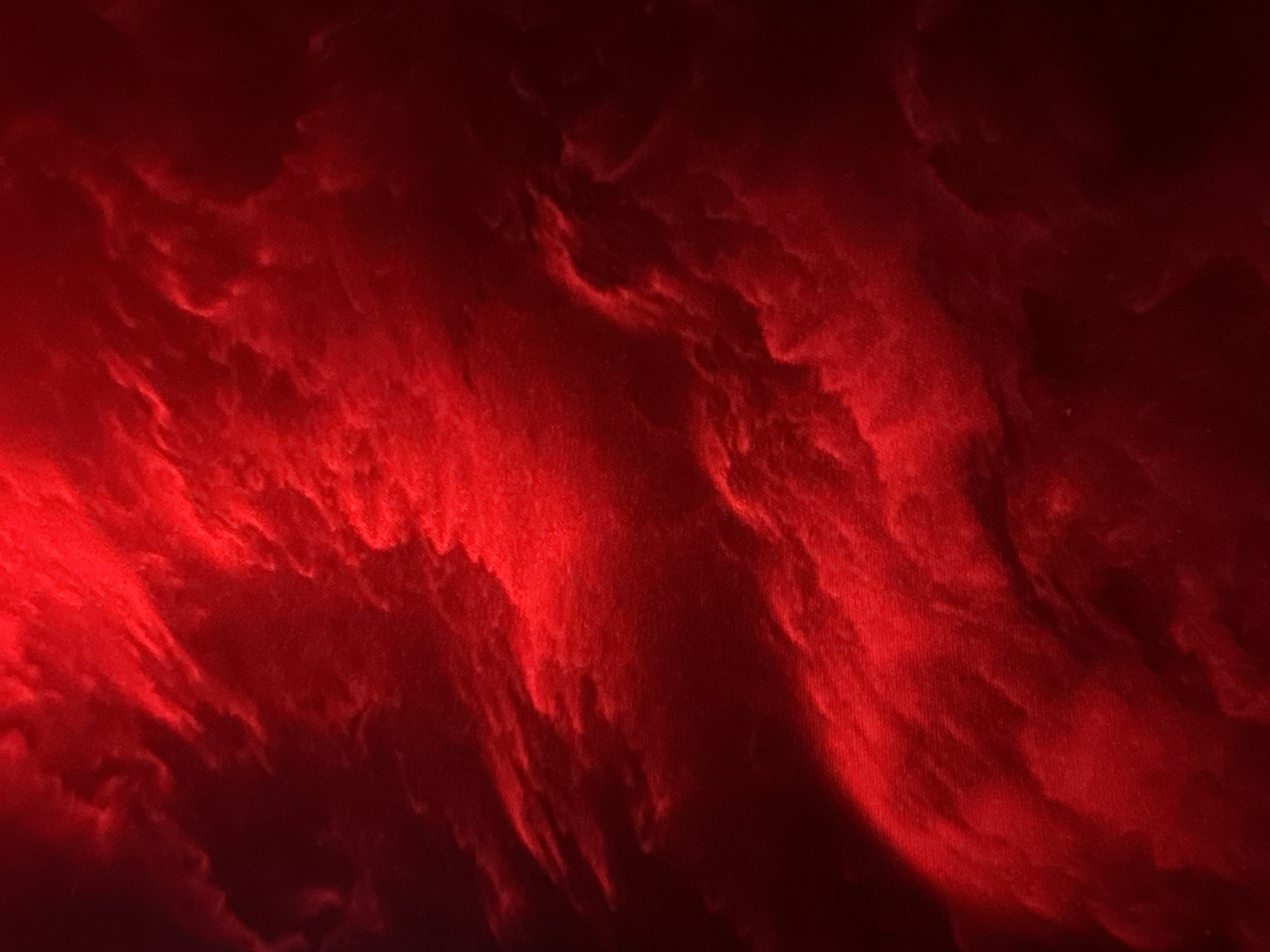 This is a photograph of a red abstract background with textured cloud-like formations. The image is predominantly red, with variations in saturation and brightness creating depth and shadow. There are no people, objects, or discernible environmental features present. The image's context within the city of Unknown, Unknown is not determinable from the visual information provided.
