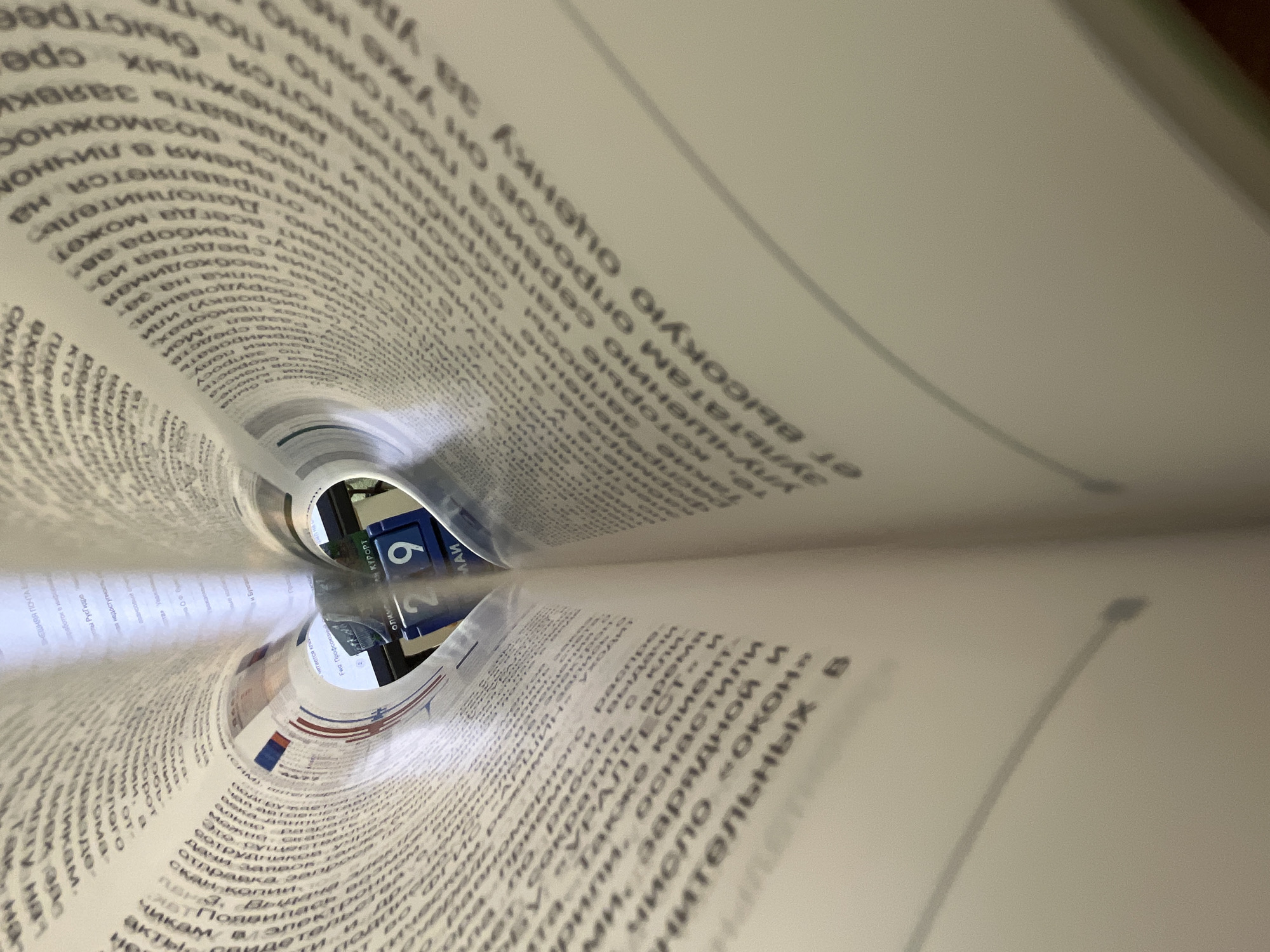 The image shows a book with its pages rolled into a tunnel shape, creating a distorted view of an area in Chaikovsky, Russia. Through the tunnel, a blue and white sign with the number 9 is visible, indicating the street number of a building. The surrounding text on the book pages appears to be in Russian.