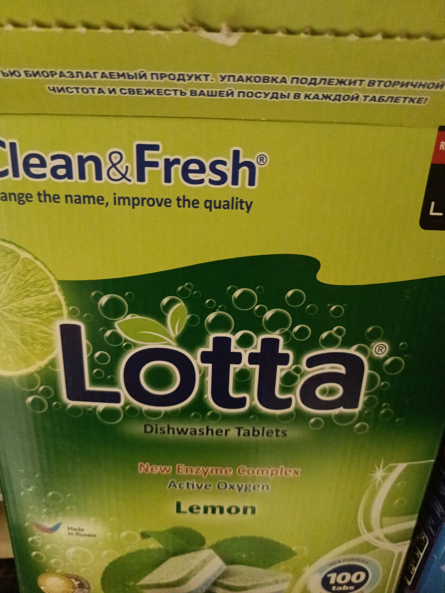 The image shows a box of dishwasher tablets. The brand name "Clean&Fresh" is visible at the top of the box, with the phrase "ange the name, improve the quality" underneath. Below this, the product name "Lotta" is displayed in large, dark letters with a green, bubbly background. The words "Dishwasher Tablets" are written beneath the name. The label also mentions "New Enzyme Complex," "Active Oxygen," and "Lemon." A slice of lemon is also visible on the box. A logo indicates the product is made in Russia. The box states that it contains 100 tablets. The box's side is also visible. There is no mention or indication of Podolsk, Russia in the image.