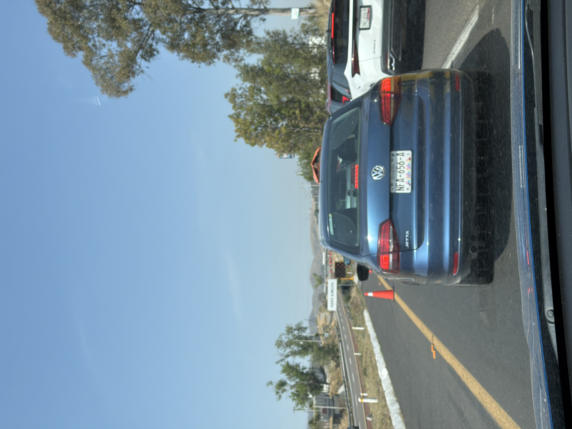 A blue Jetta with the license plate NFA-656-A is on a highway, behind a white car. The cars are near the "Puente A Moloya" sign. The location is near San Bernardino Tlaxcalancingo, Mexico.