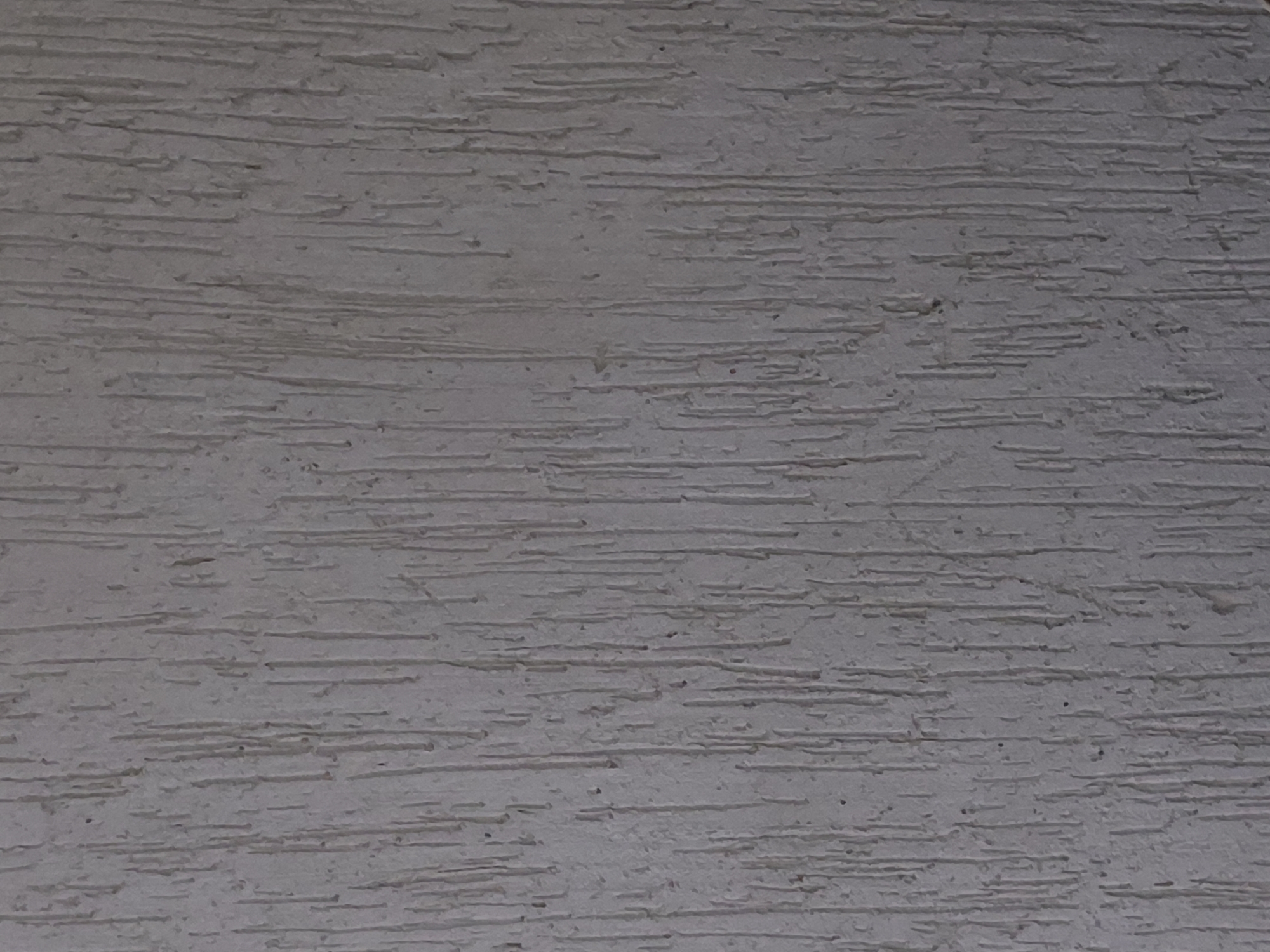 The image shows a close-up of a wall with a textured, linear finish. The surface is light gray and appears to have a rough texture with horizontal striations. There is no indication of the location being in Santa Ana, Venezuela, or any other city. The image does not show people, subjects, objects, actions, or interactions. The environment is limited to the surface of the textured wall.