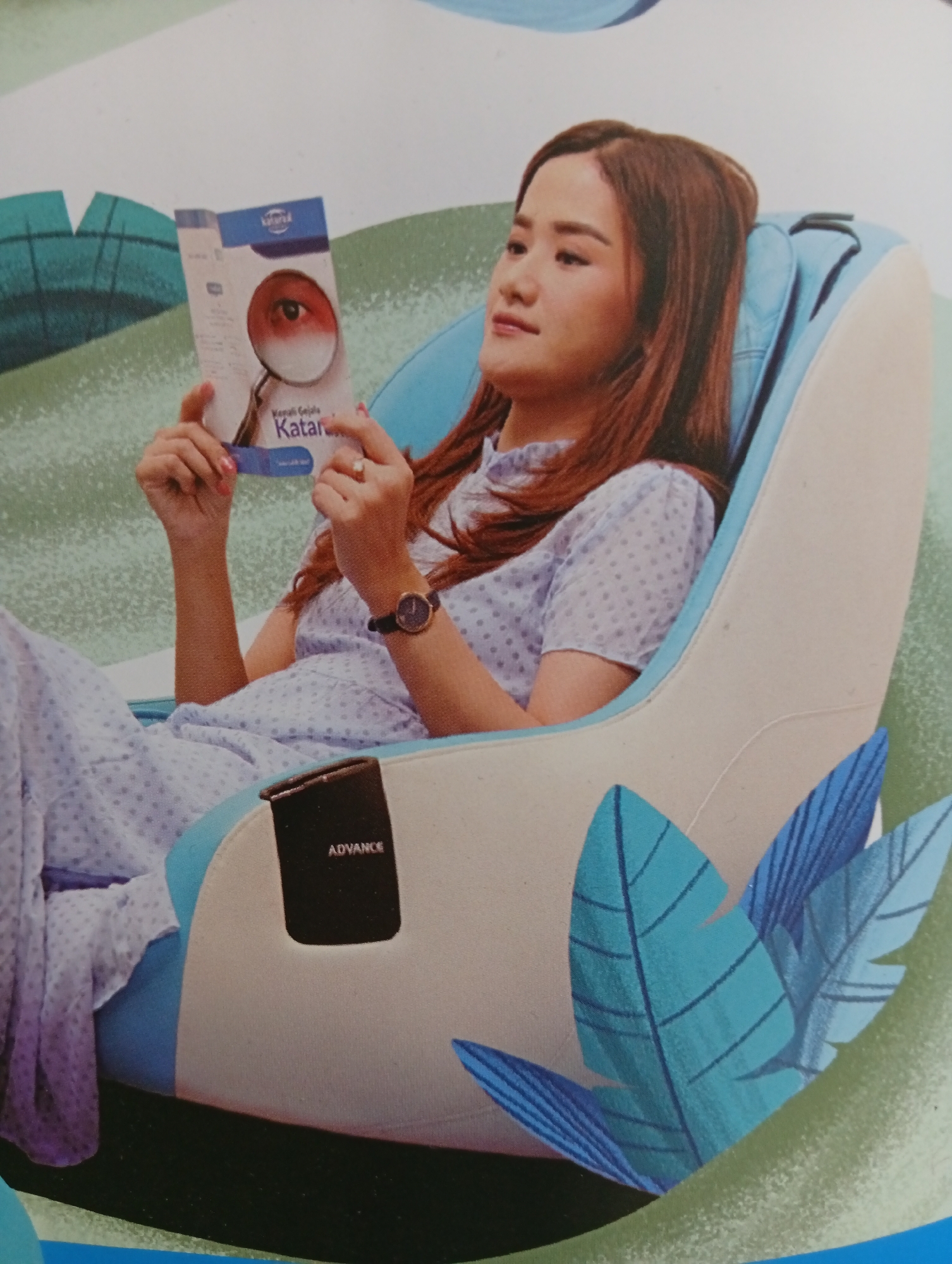 A young woman with long, dark brown hair is sitting in a light blue and white massage chair, holding a pamphlet. She is wearing a light blue dress with a white polka dot pattern and a watch with a black band on her left wrist. The pamphlet she is holding features an image of an eye magnified by a loupe and the words "Kenali Gejala Katar" in Indonesian. A dark rectangular panel with the word "ADVANCE" written on it is visible on the side of the massage chair. The background of the image is a stylized illustration with green and light blue elements, possibly representing nature or a park. The scene is indoors, as indicated by the artificial lighting and the context of the massage chair. This image is not located in Tlogomulyo, Indonesia, as there is no information in the image to suggest a specific location.