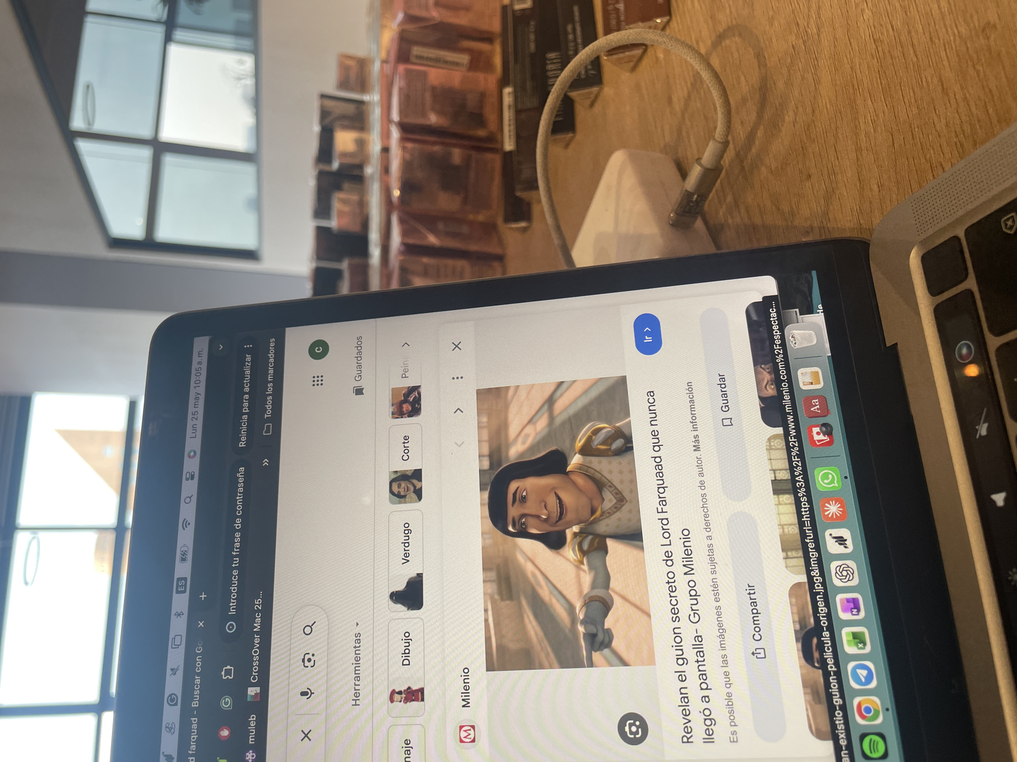 The image shows a laptop screen displaying a Google search result for "Lord Farquaad" from the movie "Shrek". The search results include an article from Grupo Milenio titled "Revelan el guion secreto de Lord Farquaad que nunca llegó a pantalla" (Reveals the secret script of Lord Farquaad that never made it to the screen). The laptop is placed on a wooden surface next to a charging cable and another laptop. In the background, there are multiple boxed items stacked on a shelf, and a window with several panes is visible. The date and time on the screen indicate "Lun 25 may 10:05 a.m." (Monday, May 25th, 10:05 AM). The location is likely somewhere in Mexico City, Mexico, due to the language used in the search results and the article from Grupo Milenio.