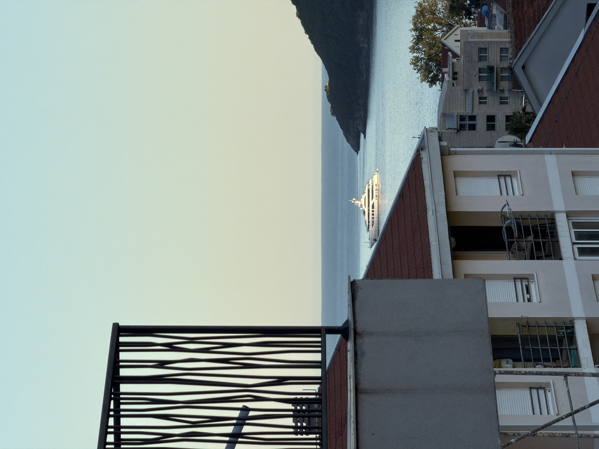 View from a rooftop in Budva, Montenegro. A yacht is visible on the Adriatic Sea. Buildings are present.