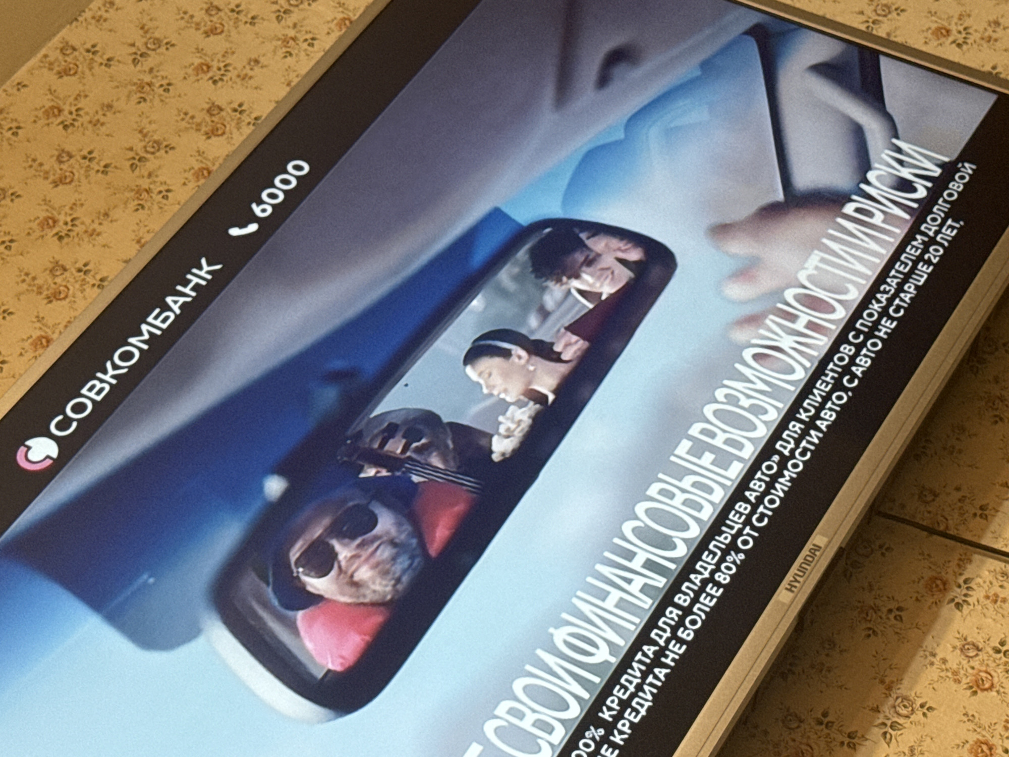 The image shows a promotional advertisement for Sovcombank, a Russian bank. The advertisement features a depiction of a car's rearview mirror reflecting a family, including a dog wearing sunglasses. Text on the advertisement highlights auto loan opportunities. The text states that the car must be no older than 20 years and the amount of credit can't exceed 80% of the vehicle cost. The brand HYUNDAI appears in the bottom corner.