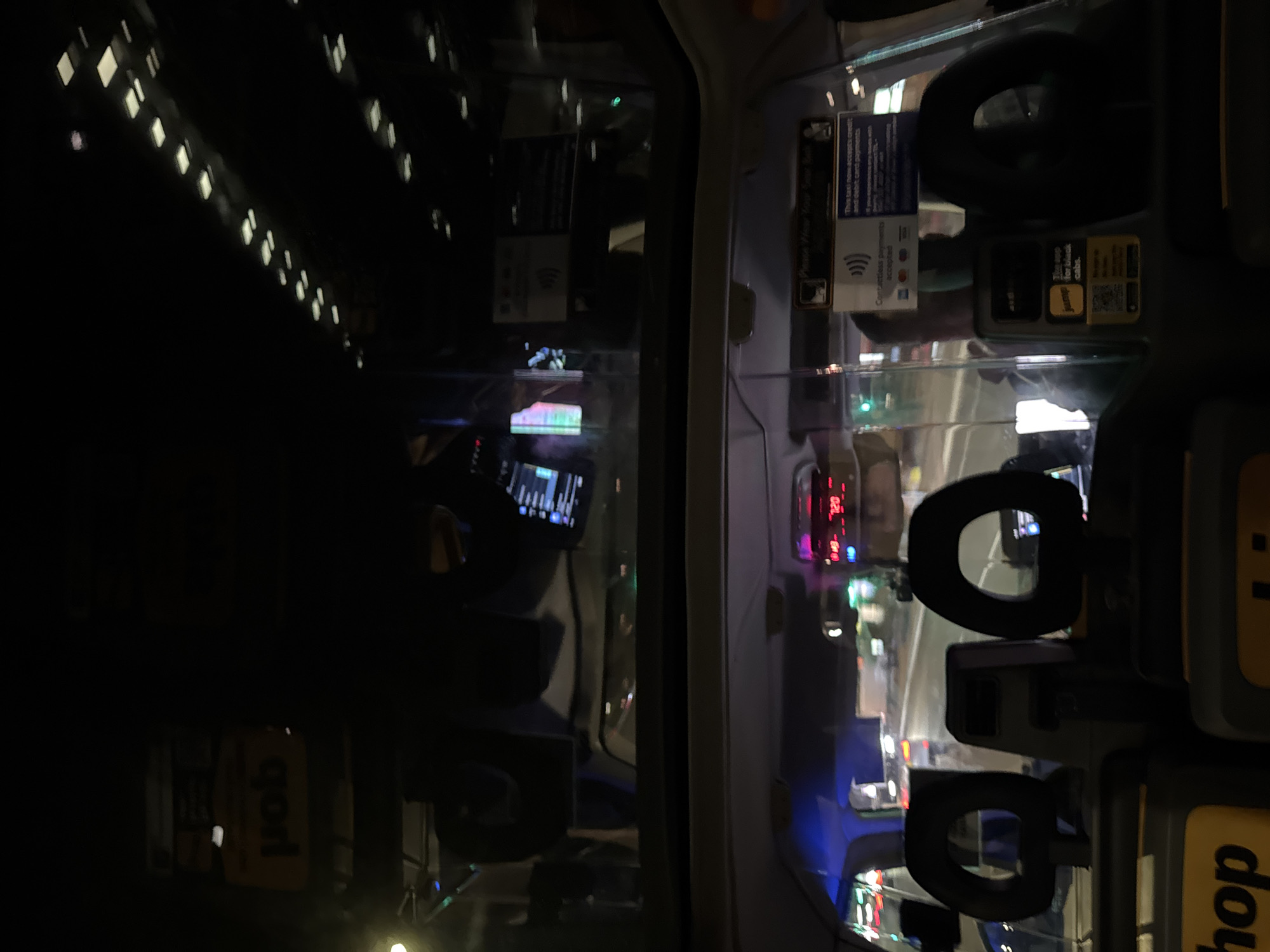 The image appears to have been taken from inside a taxi cab at night. The interior of the cab is visible, including signs regarding payment methods. Through the cab window, the lights of what appear to be city buildings can be seen. The reflection in the glass shows the city at night and it is heavily blurred. The OCR shows "hop" and "contactless payments accepted" which indicates this is in London, United Kingdom.