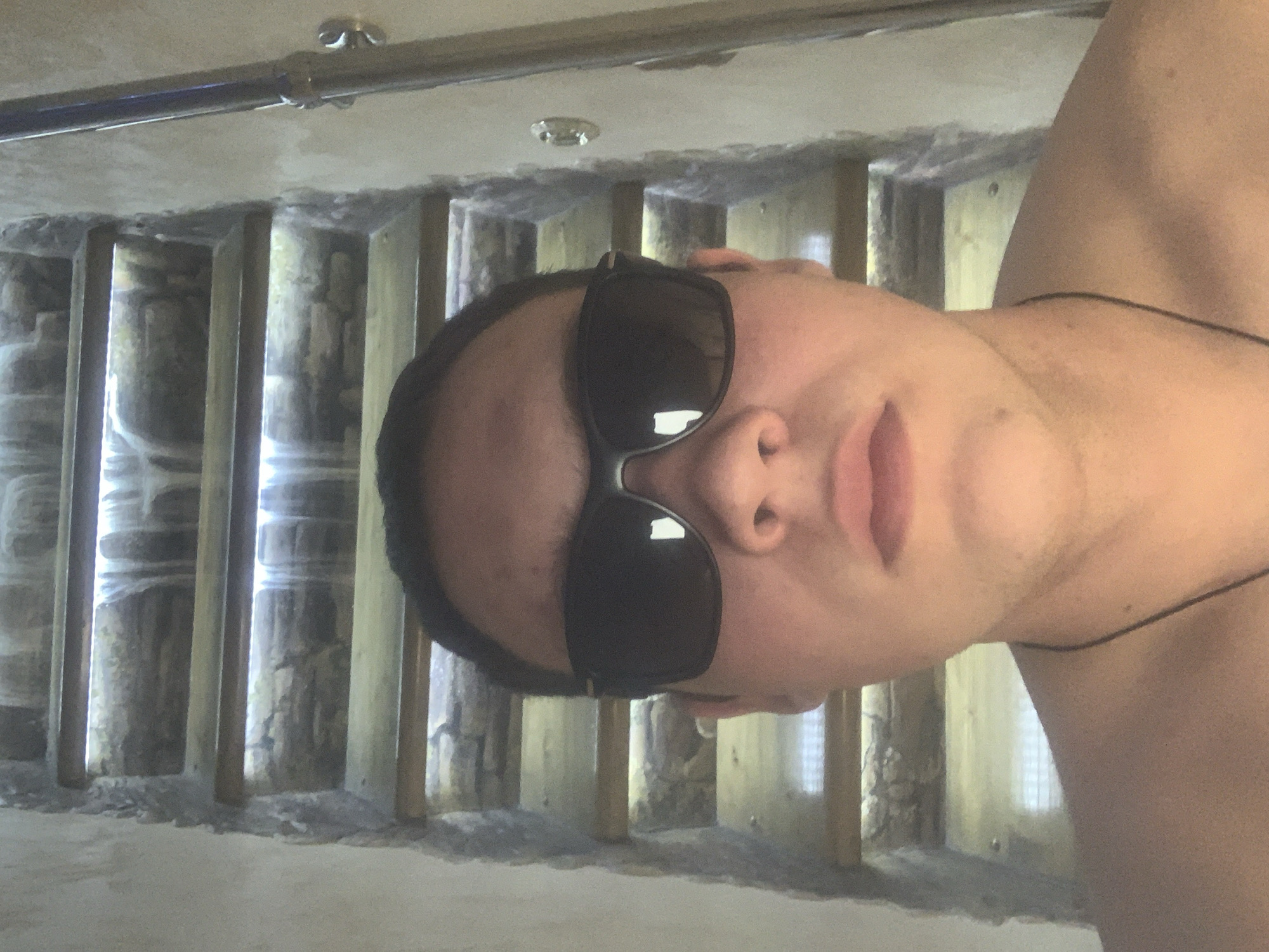 A person wearing sunglasses is the central subject of the image. They are positioned against a background featuring what appears to be a grate with light shining through, possibly a sewer or other subterranean structure. A pipe and some kind of fitting are visible in the upper portion of the scene. It's not possible to confirm the location as Severodvinsk, Russia from the image alone.