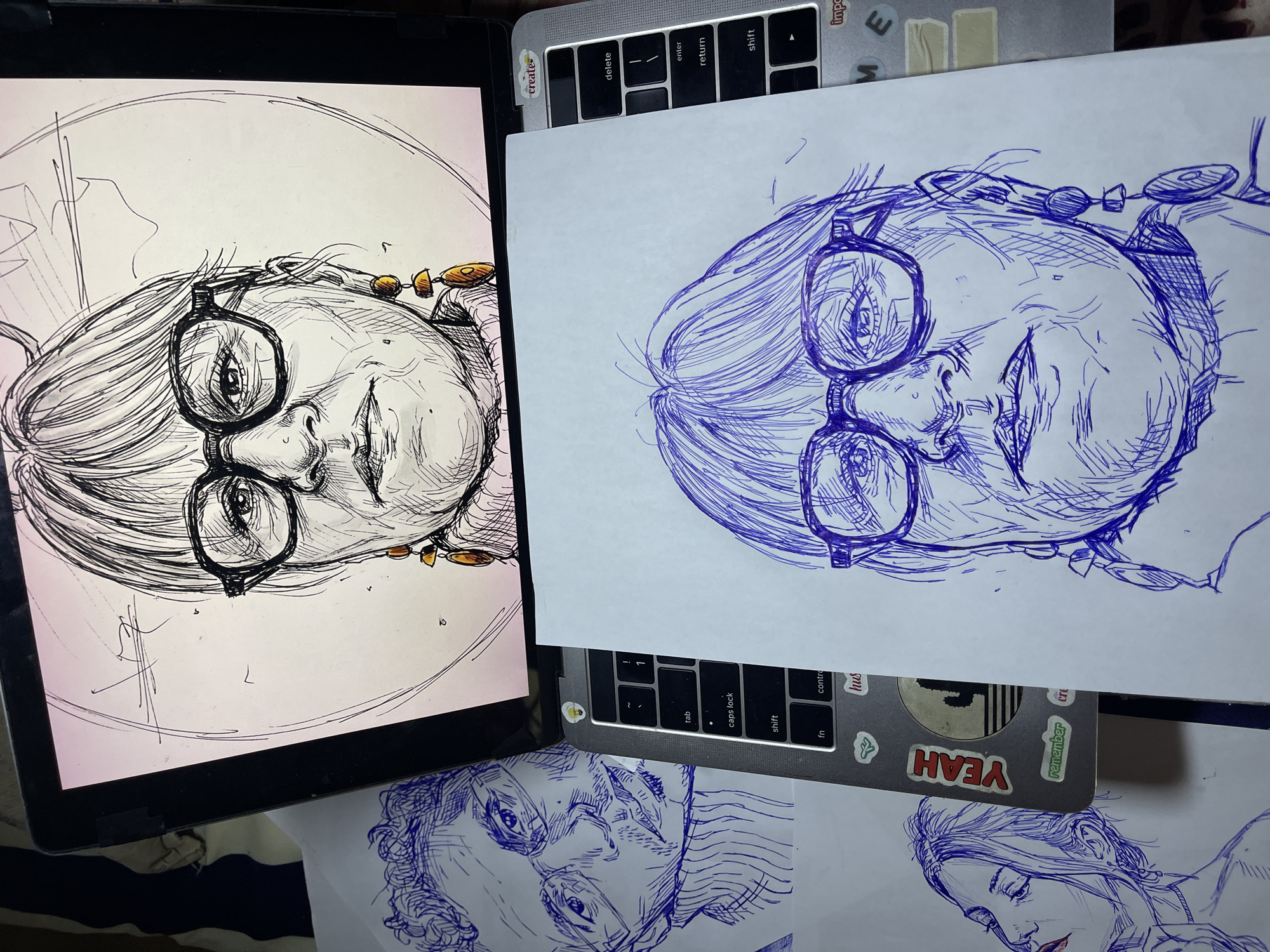 The image displays a close-up view of two pen-and-ink sketches of women, placed on top of a laptop. The sketch on the left is of a woman with curly hair and glasses, while the sketch on the right is a portrait of a woman with glasses and large earrings. The laptop's keyboard is partially visible, showing keys like "tab," "caps lock," "shift," and "enter." There are stickers on the laptop, including one that says "YEAH." The overall setting appears to be an indoor workspace, with the sketches and laptop arranged on a surface. There is no indication of the city of Jos, Nigeria, or any specific environmental details that would place the scene there.