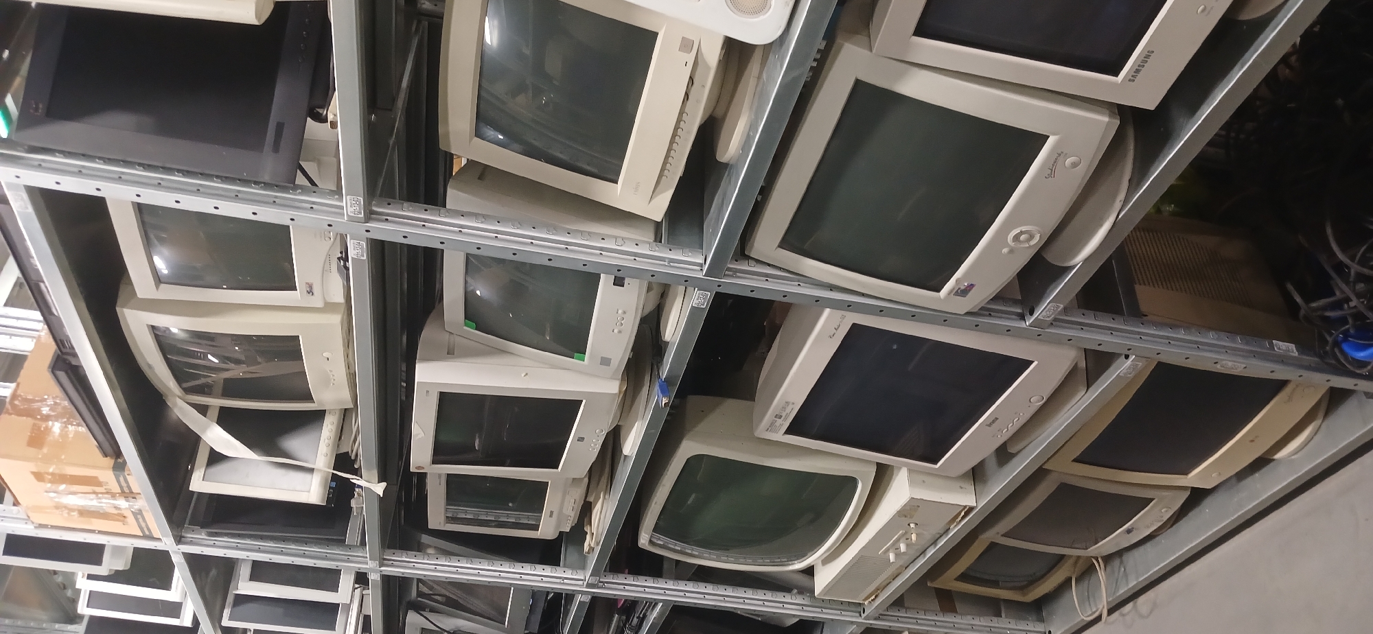 The image depicts a storage area, potentially in Moscow, Russia, filled with numerous cathode-ray tube (CRT) computer monitors stacked within a metal shelving unit. The monitors appear to be old and likely obsolete, possibly destined for recycling or disposal. No people are visible in the image.