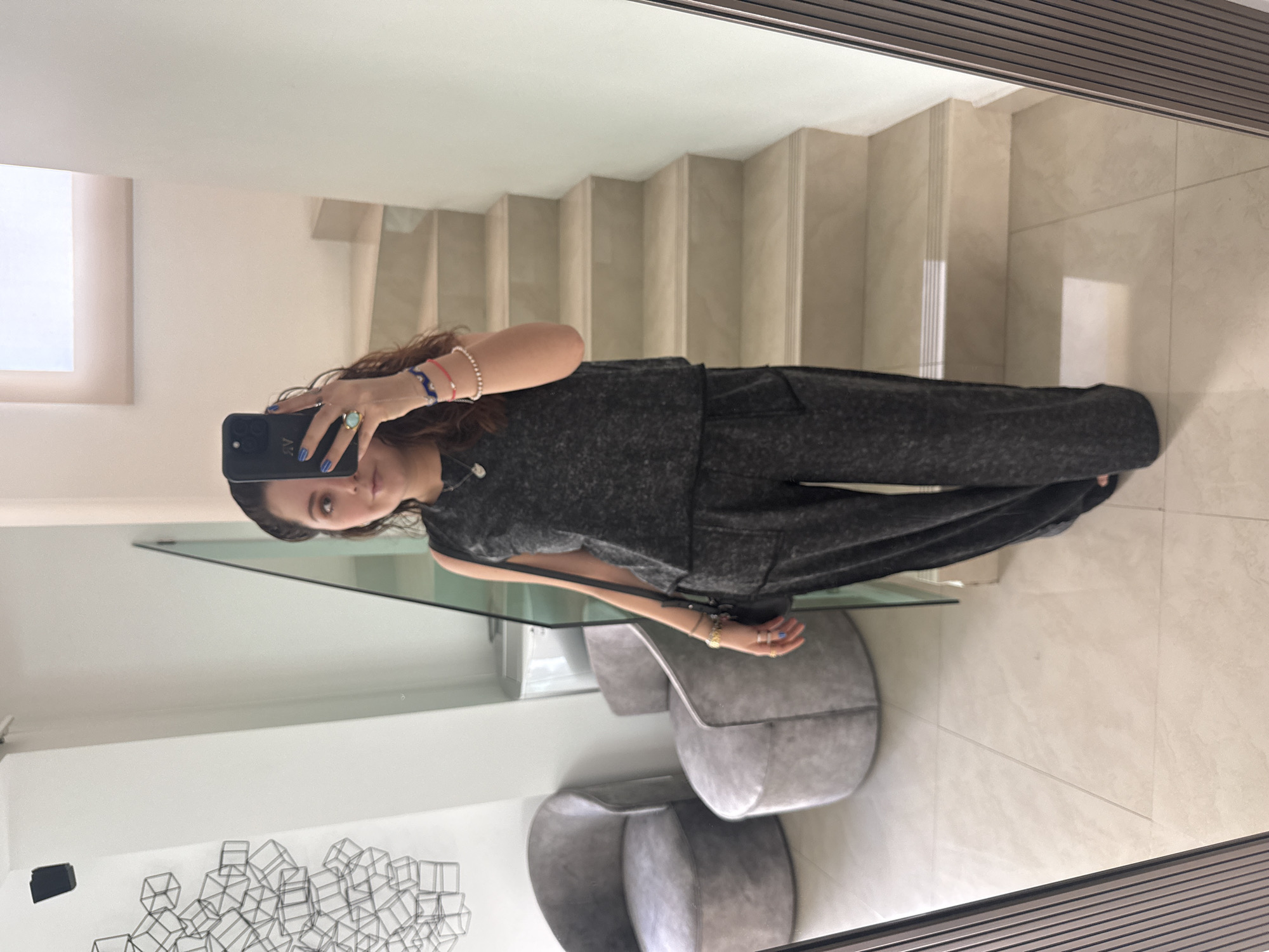 A woman is standing in front of a mirror, taking a selfie with a black phone. The background shows a modern interior, including stairs and minimalist decor. The location is Santa Clara Ocoyucan, Mexico.