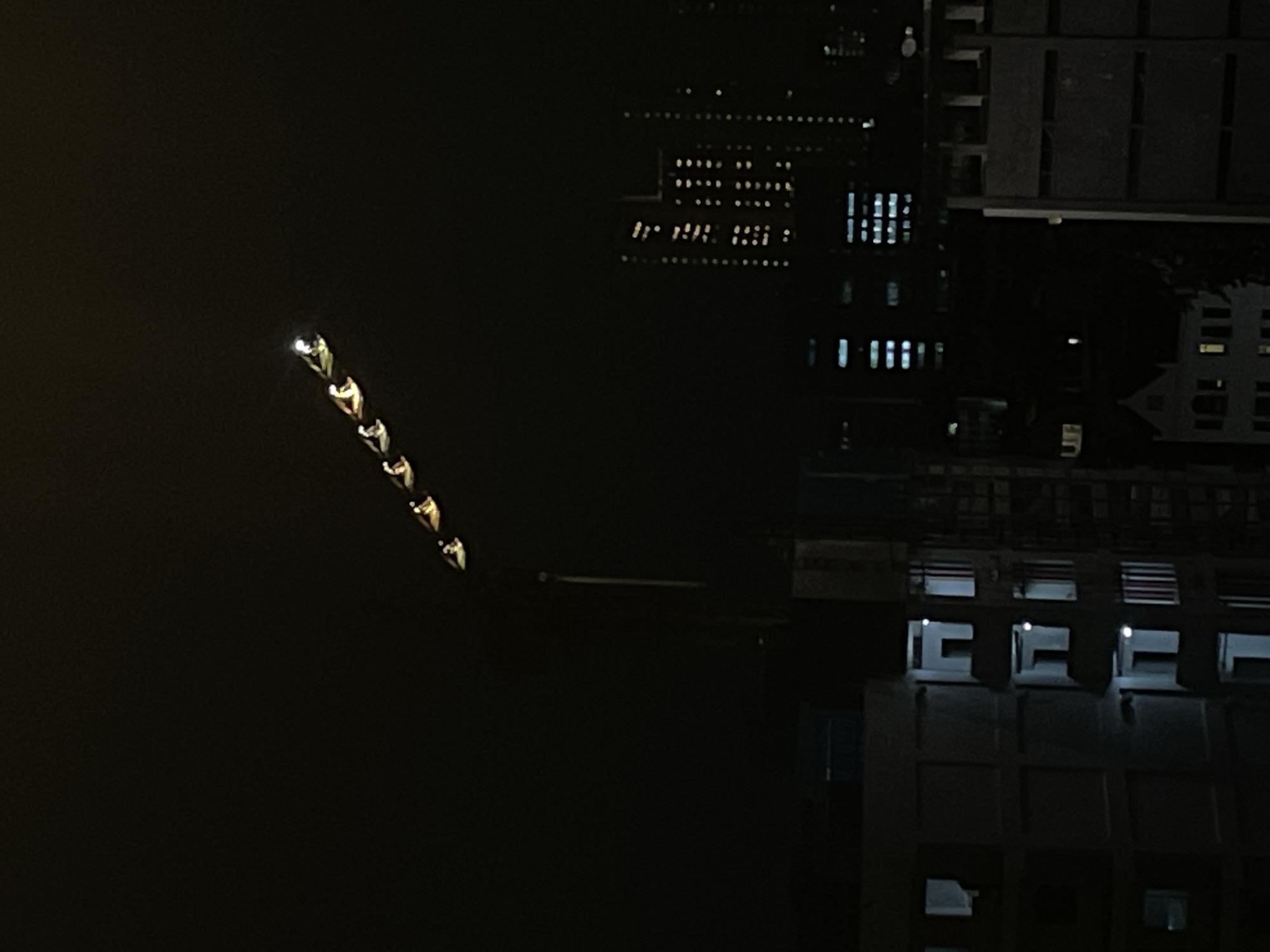The image presents a night view in Central Jakarta, Indonesia, where buildings are under construction, and a crane is stationed. The crane is noticeable due to its series of lights, marking its path. In the background, the blurred lights of other buildings suggest a bustling urban environment. The focus is mainly on the construction site, with the unlit surrounding areas providing contrast. The scene is quiet, with no visible human activity.