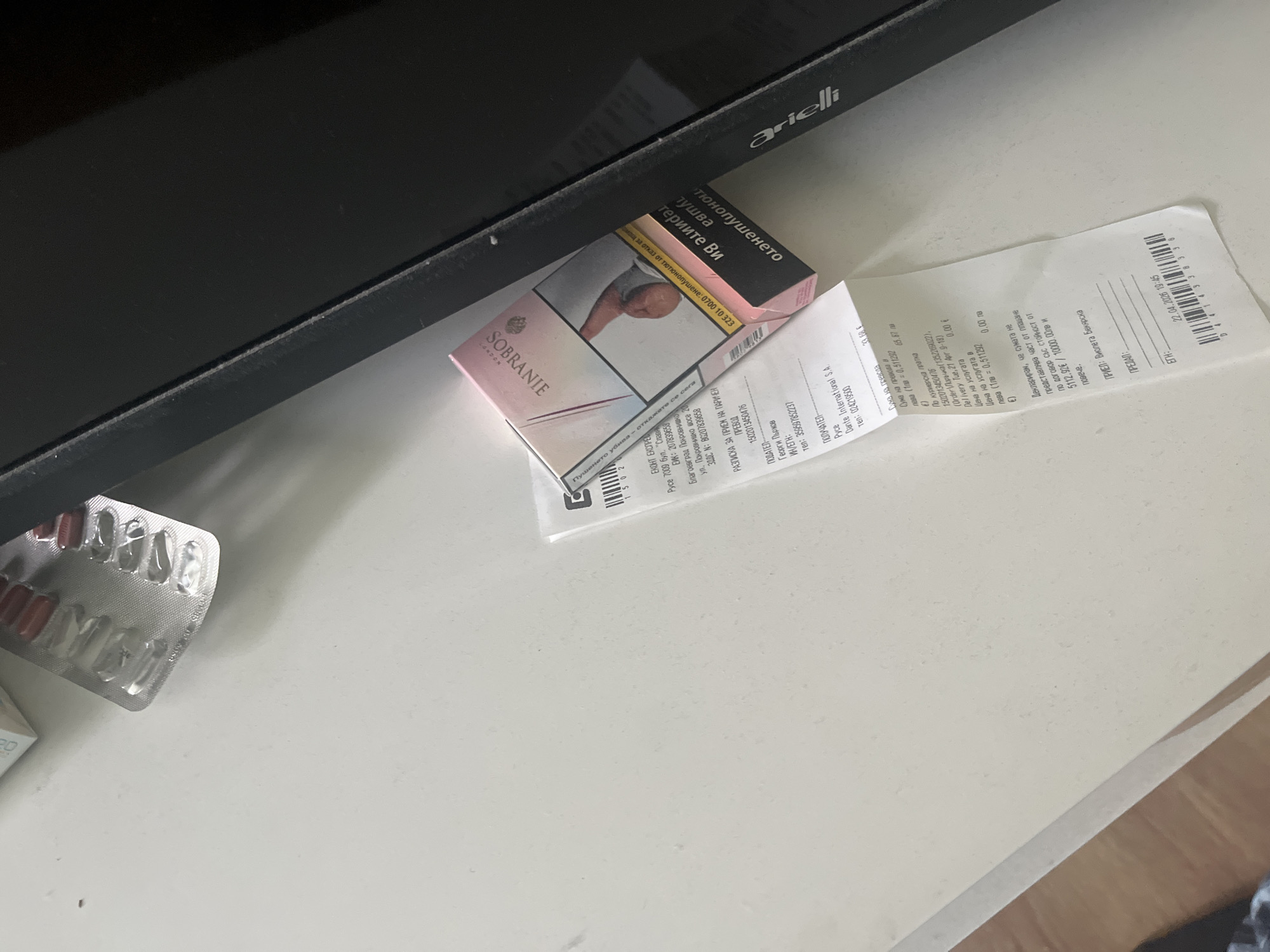 The image depicts a countertop with several items: a black Arielli-branded TV, a pink Sobranie cigarette pack, a receipt, and a blister pack of pills. The receipt appears to be for a money transfer received by Georgi Pärkov from Dante International S.A., dated April 22, 2026, for 33.68 EUR. The receipt indicates that the money transfer is associated with the Econt Express courier service in Ruse, Bulgaria, and references the Pokrovnishko Shosse 20 address in Pokrovnik near Blagoevgrad, Bulgaria. The scene is indoors.