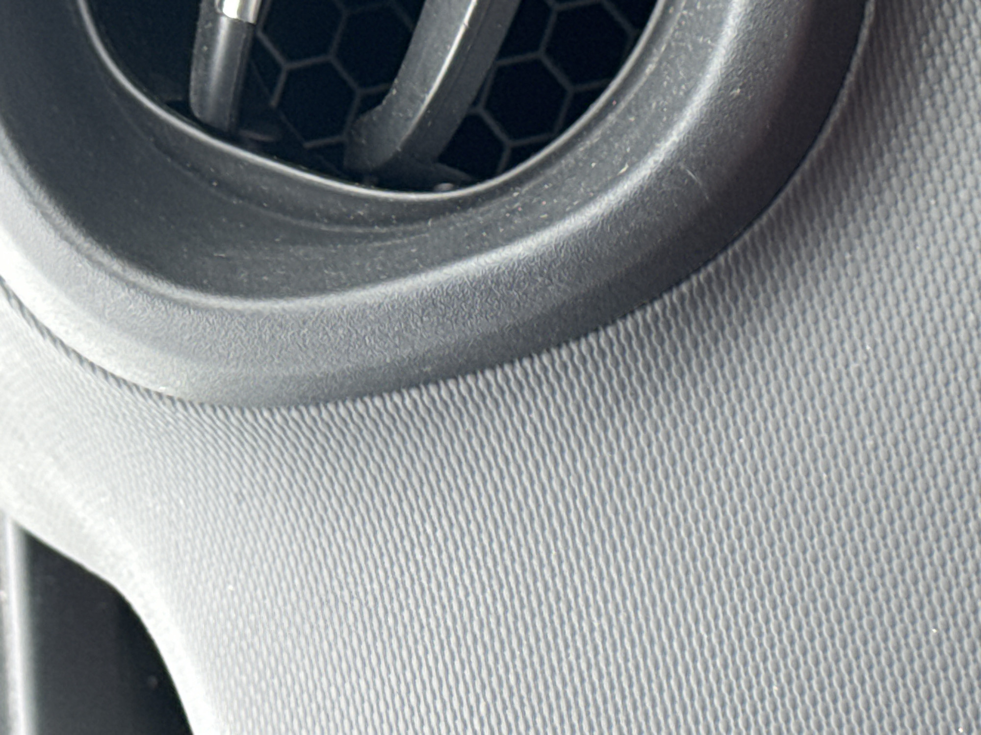 The image shows a close-up view of a car's interior, specifically focusing on a textured dashboard and an air vent. The dashboard has a ribbed, matte grey finish, creating a visually complex surface. To the right, a black plastic surround frames the air vent. The vent itself features a honeycomb pattern behind adjustable louvers. The overall lighting suggests an indoor or shaded environment, possibly within a vehicle. There are no people or animals present in the image, and no overt actions or interactions are depicted. The location in Cottrellsrath, Ireland, is not visually evident from the image content.