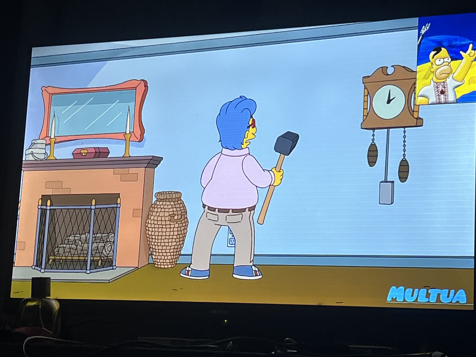 The image depicts a scene from an animated television show, likely "The Simpsons," featuring a character with blue hair and glasses holding a sledgehammer. The character is standing in what appears to be a living room with a fireplace, a mirror above the mantelpiece, and a cuckoo clock on the wall. A small inset in the upper right corner shows Homer Simpson with the Ukrainian flag in the background. The bottom right corner of the screen displays the text "MULTUA." The overall setting is an indoor environment rendered in a cartoonish style. There is no indication of the specific location within the city of Zoriane, Ukraine, or any interaction with the environment beyond the character's stance with the sledgehammer.