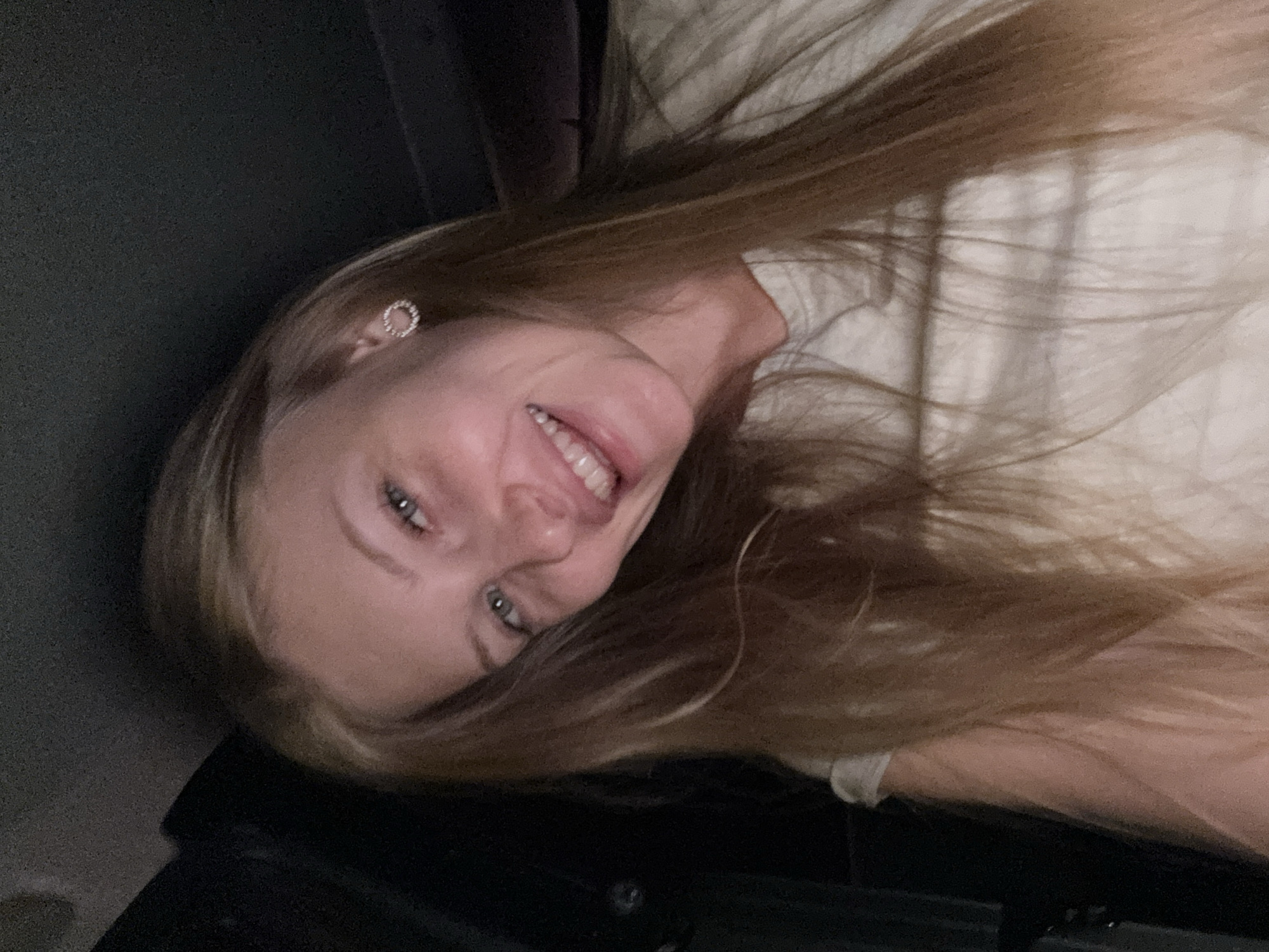 A young woman with blonde hair and blue eyes is pictured in a selfie. She is wearing a light-colored t-shirt and has a sparkling circular earring in her left ear. The background is dark, suggesting an indoor setting or nighttime. The image does not contain any information indicating it was taken in the city of Perm, Russia.