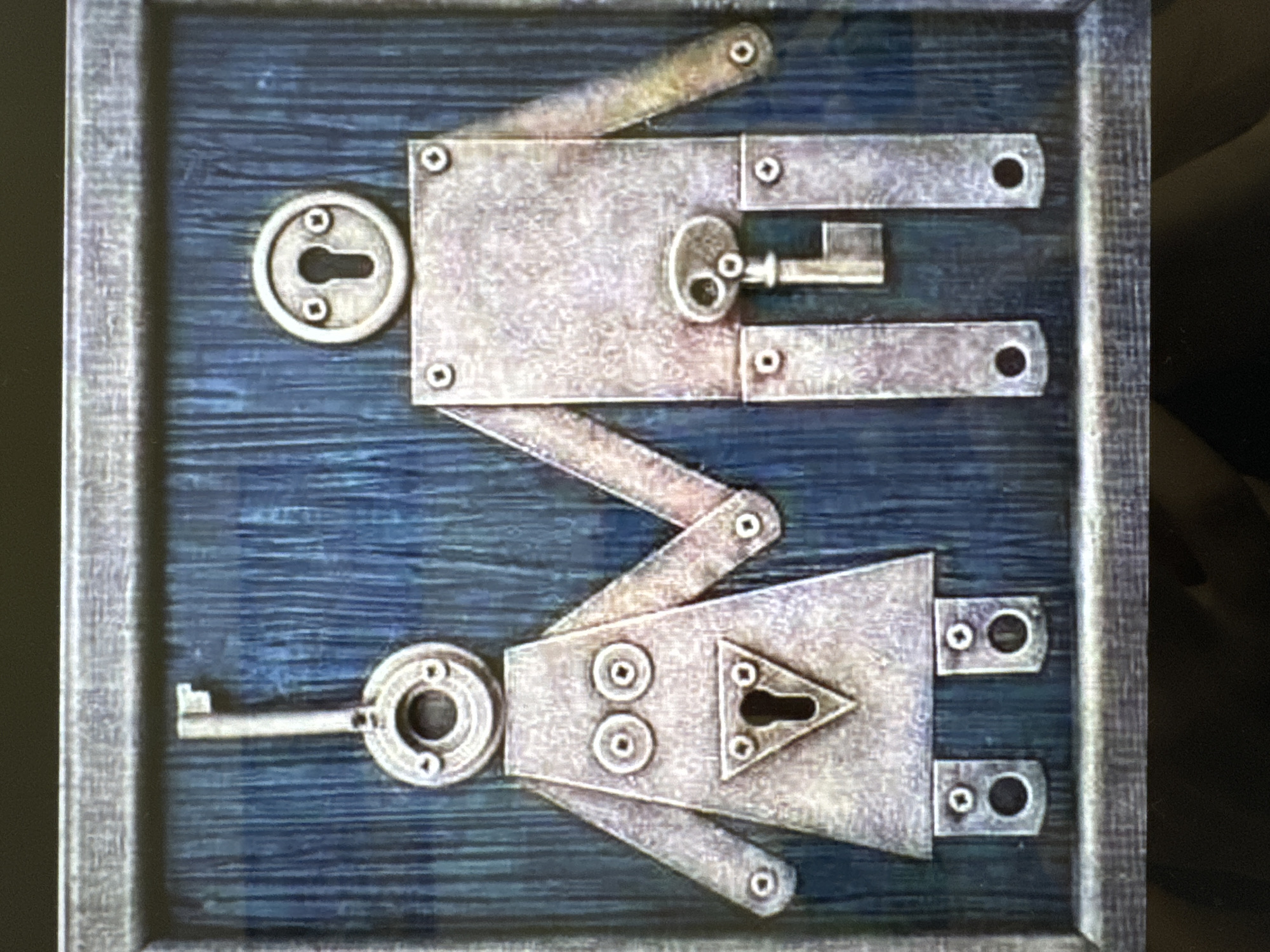 The image shows a framed decorative artwork with a rustic, metallic aesthetic. The artwork depicts two stylized figures, resembling a couple, constructed from metal parts. The figure on the left, interpreted as female, has a key as its head, a triangular metal plate with a keyhole for its torso, and circular metal pieces for eyes. The figure on the right, interpreted as male, has a keyhole as its head, a rectangular metal plate for its torso with a key inserted into a keyhole shape positioned in the groin area, and a key as its dangling element. Both figures have articulated limbs made of metal strips and are joined at the hands. They are standing against a dark blue, wood-grained background. The artwork is framed by a textured, gray border. The overall impression is one of a symbolic representation of partnership or marital union, using lock and key motifs.
The image does not contain any identifiable information about its location in the city of Yalta, Ukraine.