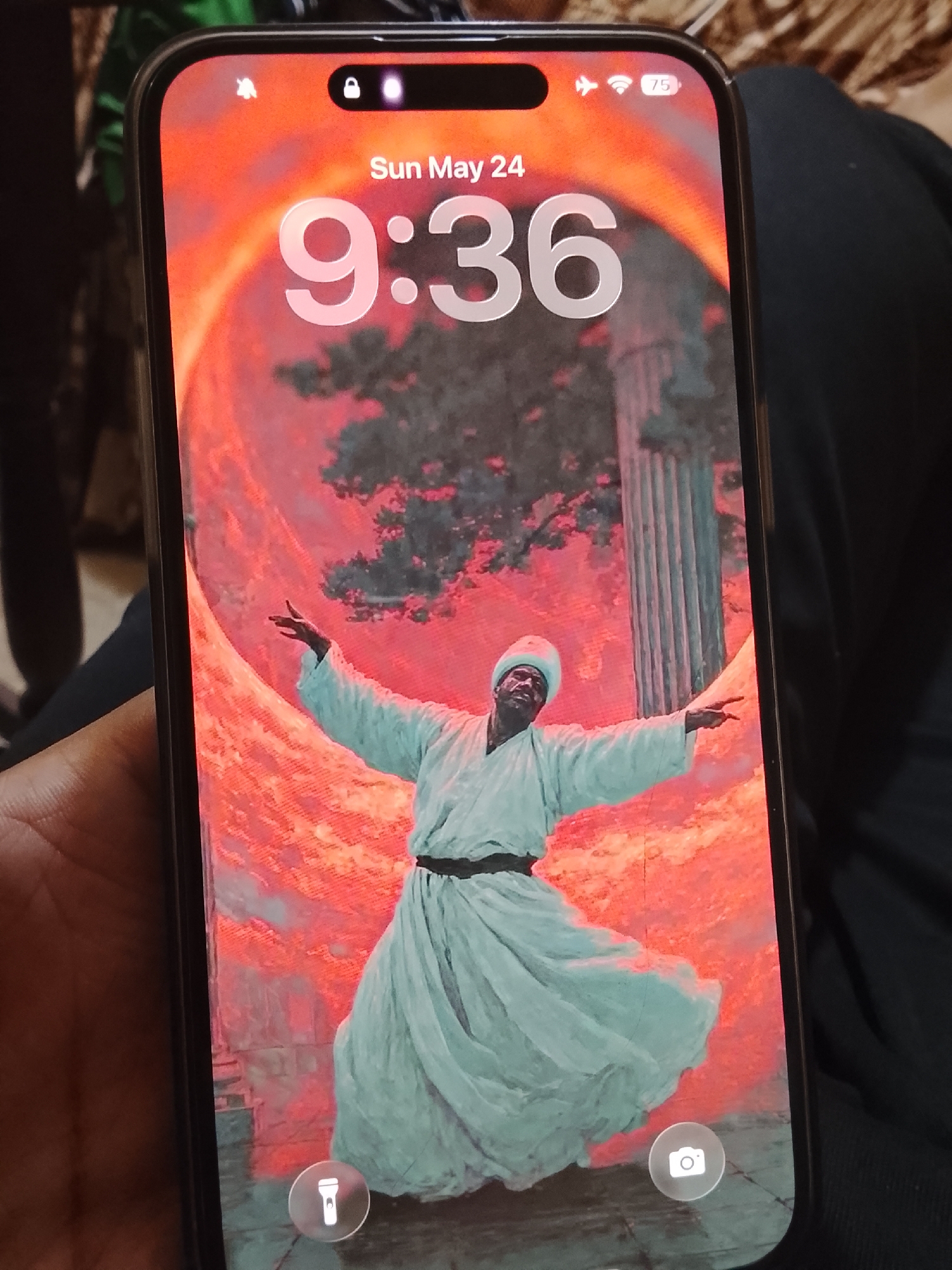 An iPhone displays a lock screen with the time "9:36" on Sunday, May 24th. The wallpaper shows a man in traditional clothing with outstretched arms. The image is likely an artistic rendering of a Sufi whirling dervish. The location in Multan, Pakistan, cannot be determined from the image.