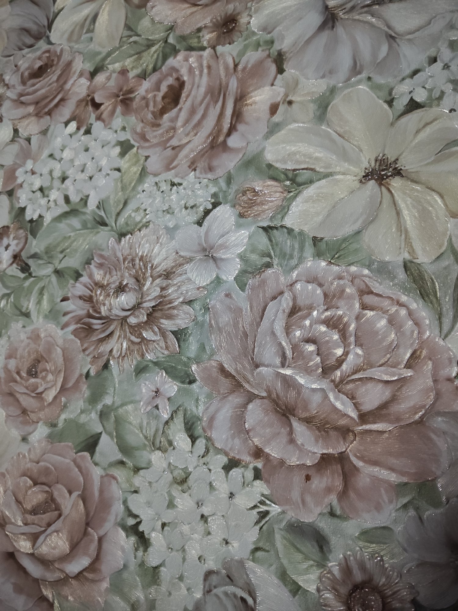 The image displays a close-up of a floral relief pattern, possibly wallpaper or a decorative wall panel. The design features various types of flowers, including roses, hydrangeas, and other blossoms, rendered in soft pastel shades of pink, cream, and light brown, with subtle green leaves. The surface appears to have a textured, three-dimensional quality, with individual petals and leaves clearly defined. There are no people, animals, or identifiable landmarks present in the image. The scene is a static, decorative composition. The location in Zaraysk, Russia, is not discernible from the visual information provided in the image.