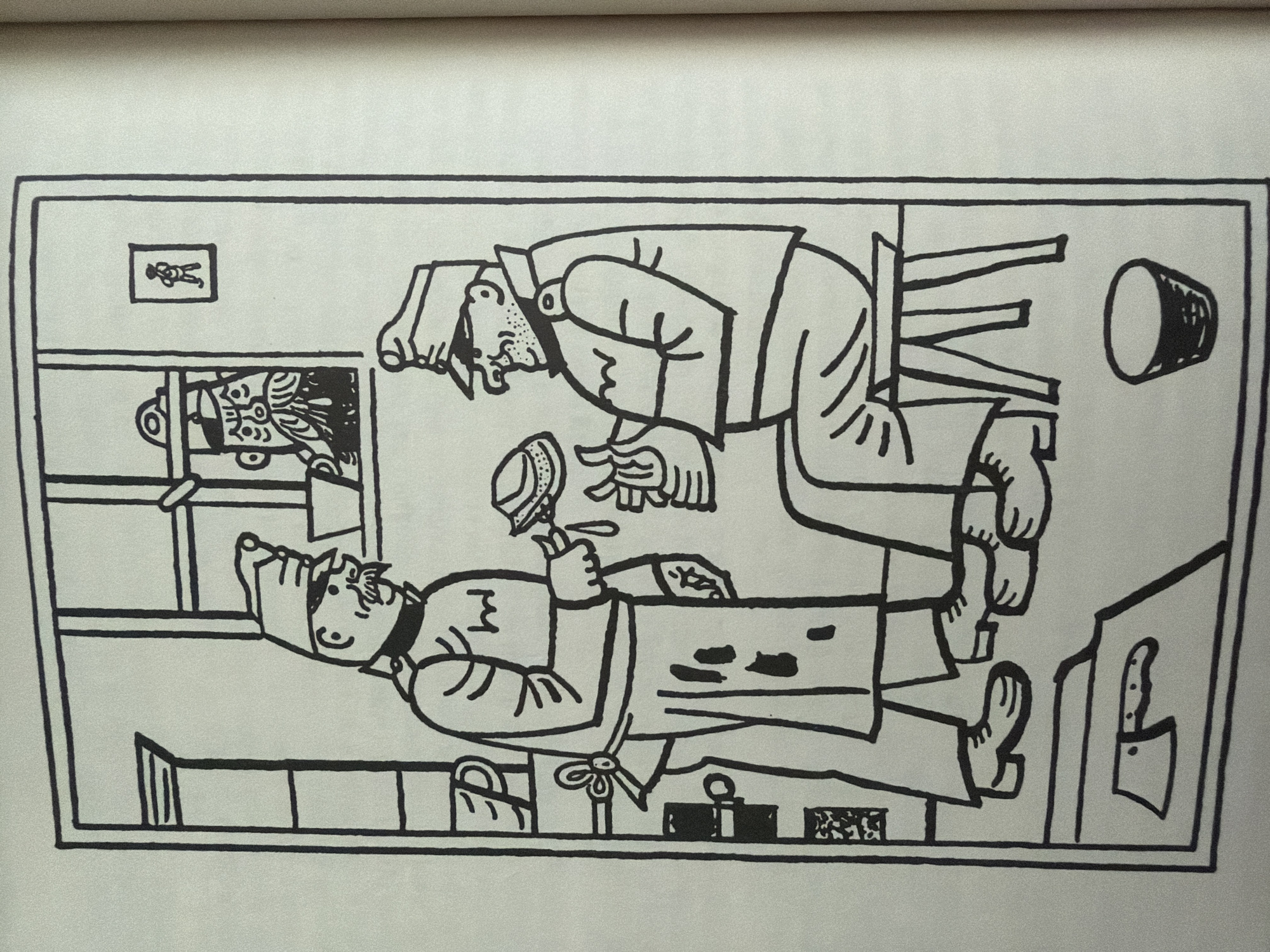 The image depicts an interior scene, possibly a kitchen or workshop, with two men in military-style uniforms. The man on the left, wearing an apron over his uniform, is holding a brush and appears to be cleaning or applying something to a hat. He has a mustache and is standing. The man on the right is seated on a stool, wearing a cap, and holding a hat in his hands, seemingly examining it. He has a beard and appears to be concentrating on the hat. In the background, a window reveals a third man with a beard peering out, wearing a cap. On the wall, a small framed picture of a figure is visible. The environment includes shelves with mugs and other containers, a stool, a bucket on the floor, and a cleaver with a knife blade lying on the ground. There is no information within the image or its context that indicates a location in the city of Pazardzhik, Bulgaria.