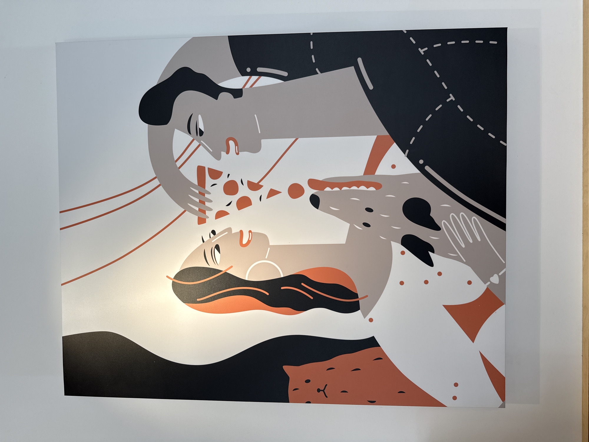 The image is a close-up shot of a framed illustration hanging on a white wall. The illustration features a stylized design of a man, woman, and dog interacting with a slice of pizza. The man is positioned above the woman, extending the pizza slice towards her. A dog is also reaching for the pizza. The style is graphic with bold colors, including black, white, gray, and a burnt orange. Below the woman, there is a black shape and an orange shape resembling a cat.
The image does not provide any specific information about the location in Tobolsk, Russia. It is simply an illustration on a wall.